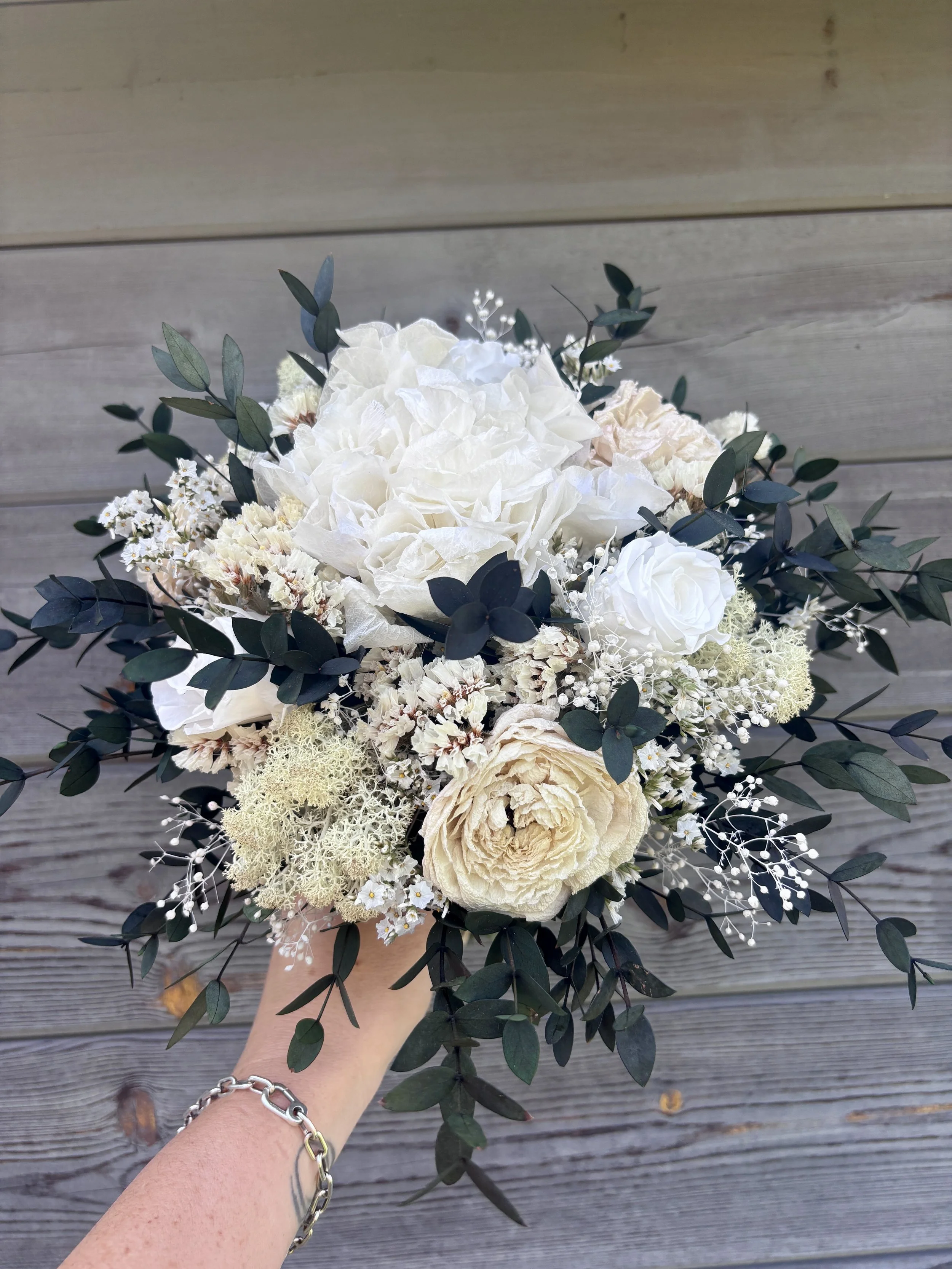 Bouquet de mariée bohème chic en fleurs séchées et stabilisées, composé de pivoines blanches, roses stabilisées, statice blanc, mousse végétale et feuillage d’eucalyptus noir. Cette création artisanale associe élégance, douceur et caractère pour un m