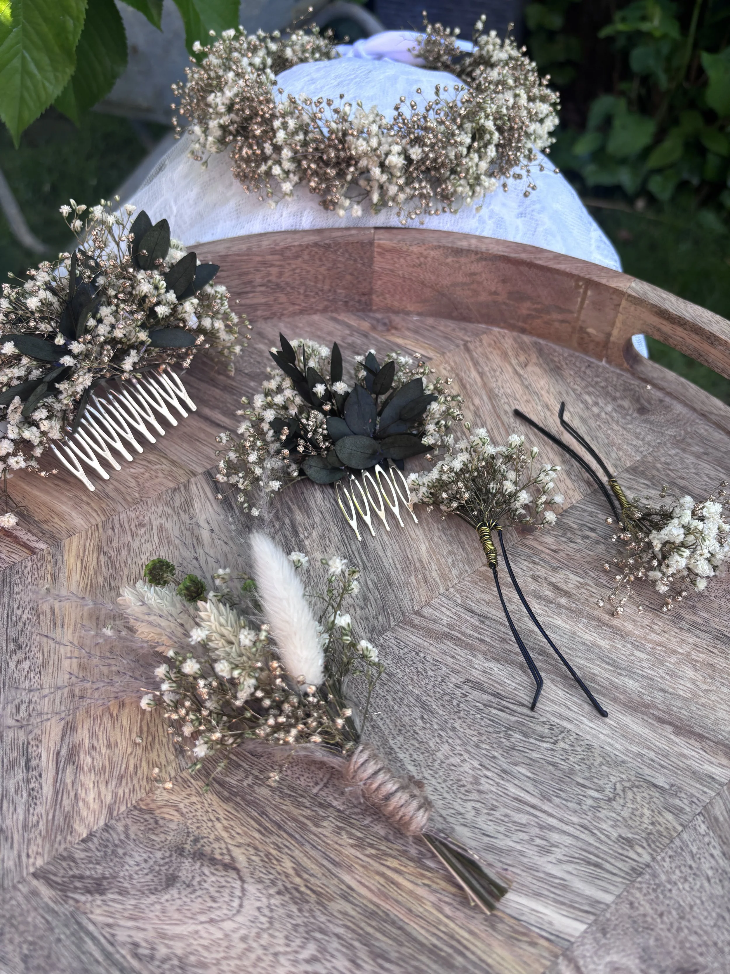 Des couronnes de fleurs blanches et vertes, avec une brosse à cheveux noire, un peigne et une autre couronne en bois sur une table en bois.