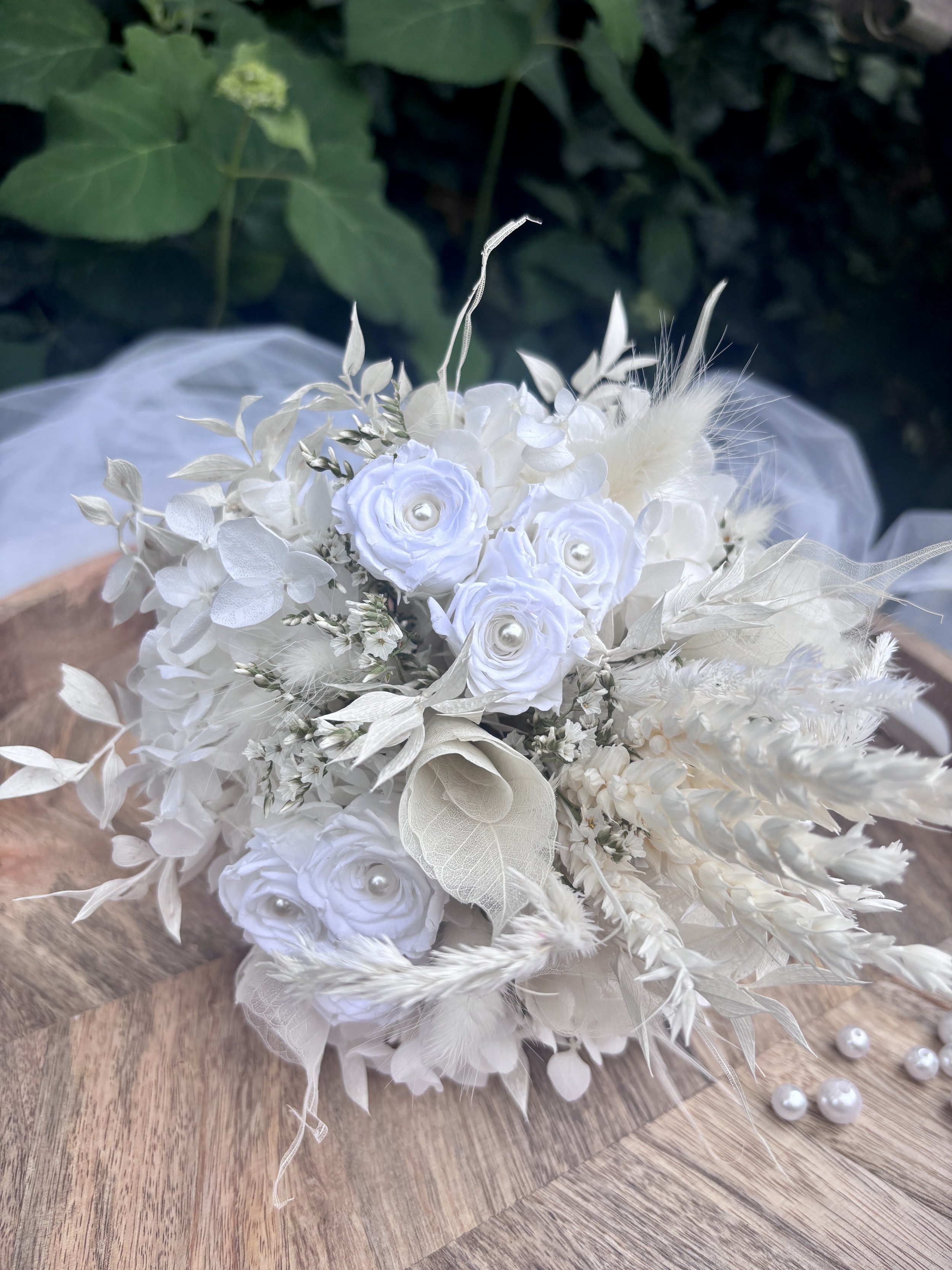 Bouquet de mariée en fleurs séchées et stabilisées blanches, réalisé artisanalement dans un esprit bohème chic et romantique. Cette création florale associe hortensias stabilisés, roses éternelles ornées de perles, arums délicats, feuillages blanchis
