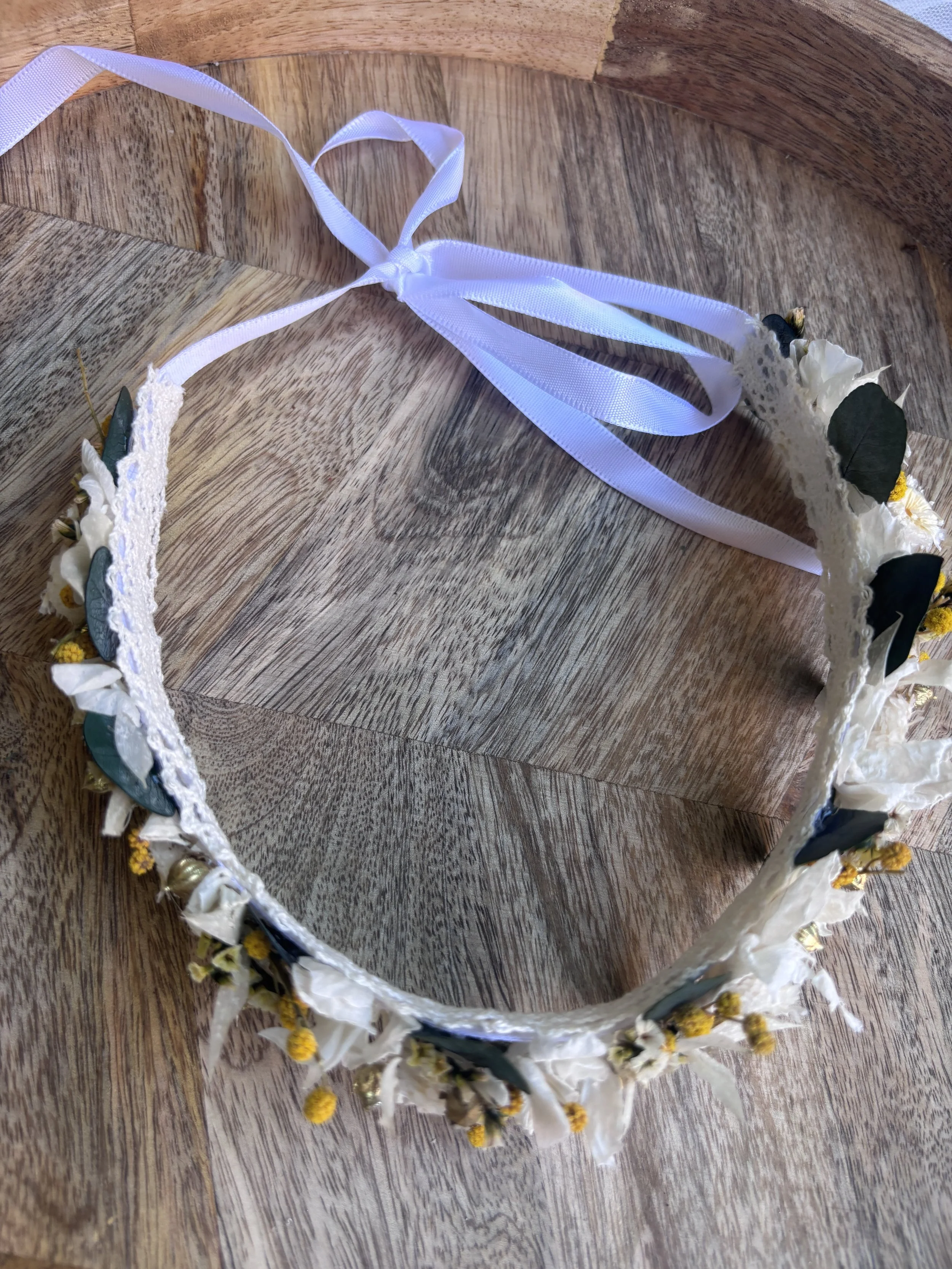 Couronne de fleurs blanches avec des feuilles vertes et des petits fleurs jaunes, posée sur une surface en bois
