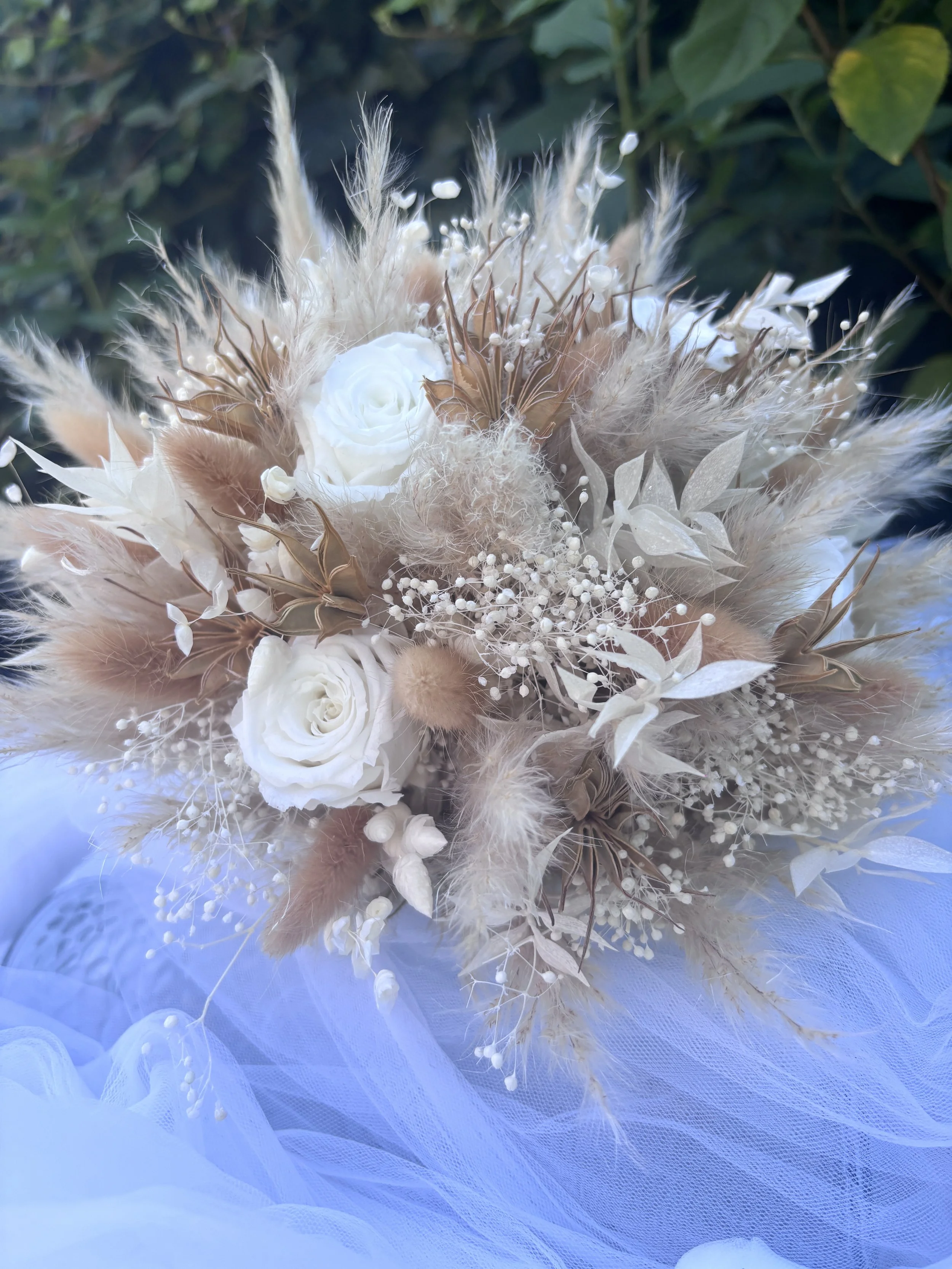 Bouquet de mariée réalisé artisanalement en fleurs séchées et stabilisées. Une création romantique et aérienne mêlant roses blanches, gypsophile, pampas et feuillages naturels dans des nuances ivoire, nude et rose poudré. Création sur mesure par L’At