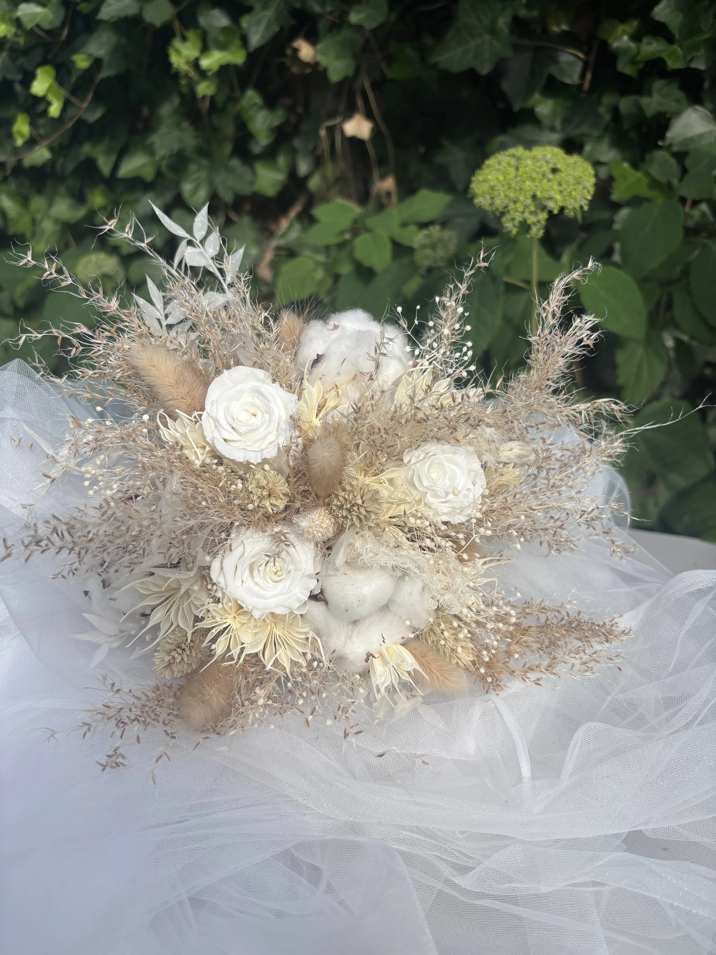 Bouquet de mariée bohème composé de fleurs séchées et stabilisées dans des tons blanc cassé, ivoire et beige naturel. Réalisé à la main par L’Atelier Fleurs & Sens à Saint-Saulve, près de Valenciennes, ce bouquet associe roses stabilisées, coton, gra