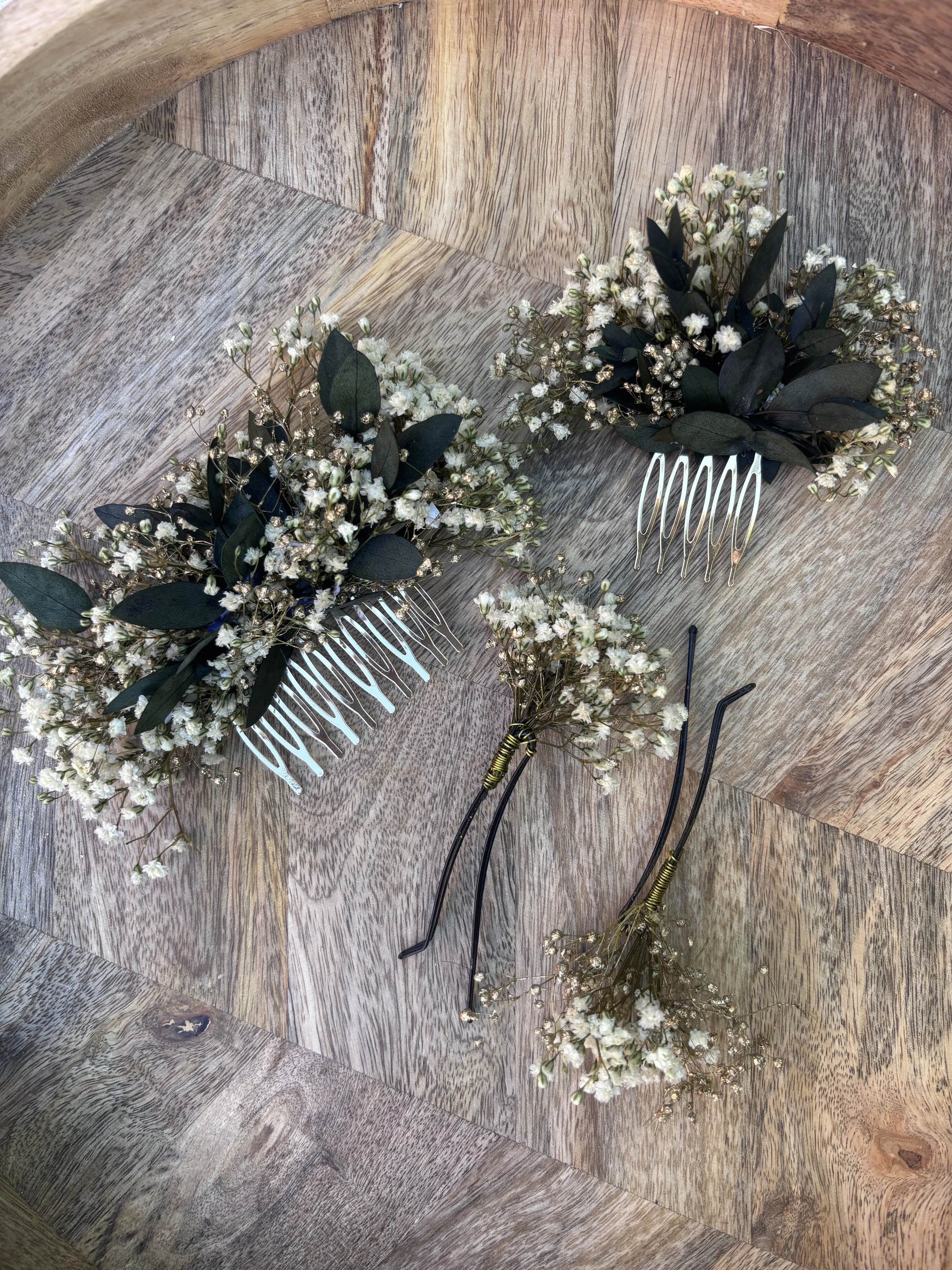 Deux coiffes de mariée avec des fleurs blanches et des feuilles vertes, posées sur une surface en bois.