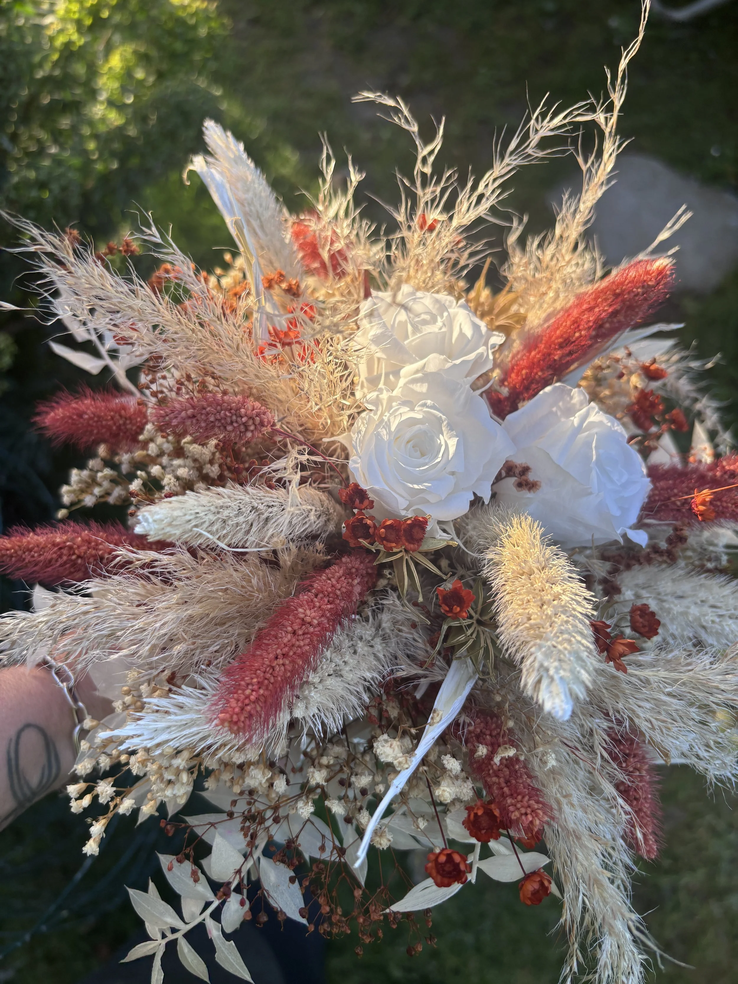 Bouquet de mariée bohème en fleurs séchées et stabilisées aux teintes terracotta, bordeaux, crème et blanc. Cette création florale artisanale associe roses éternelles blanches, pampas, setaria, graminées naturelles et délicates fleurs séchées pour of