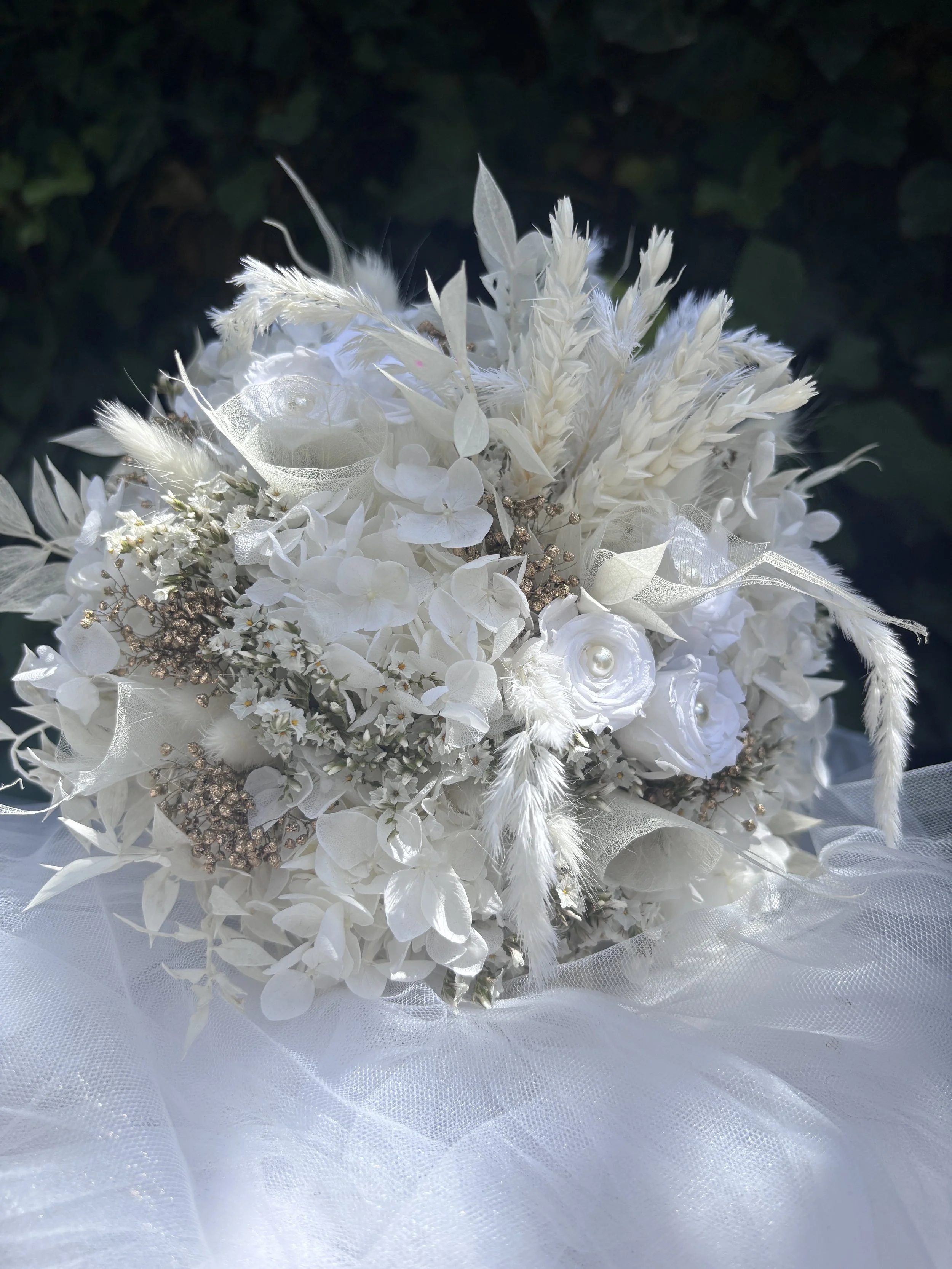 ce bouquet de mariée en fleurs séchées et stabilisées associe hortensias blancs, roses stabilisées, graminées aériennes et délicates touches nacrées pour un rendu élégant, romantique et intemporel. Réalisé à la main dans mon atelier à Saint-Saulve, p