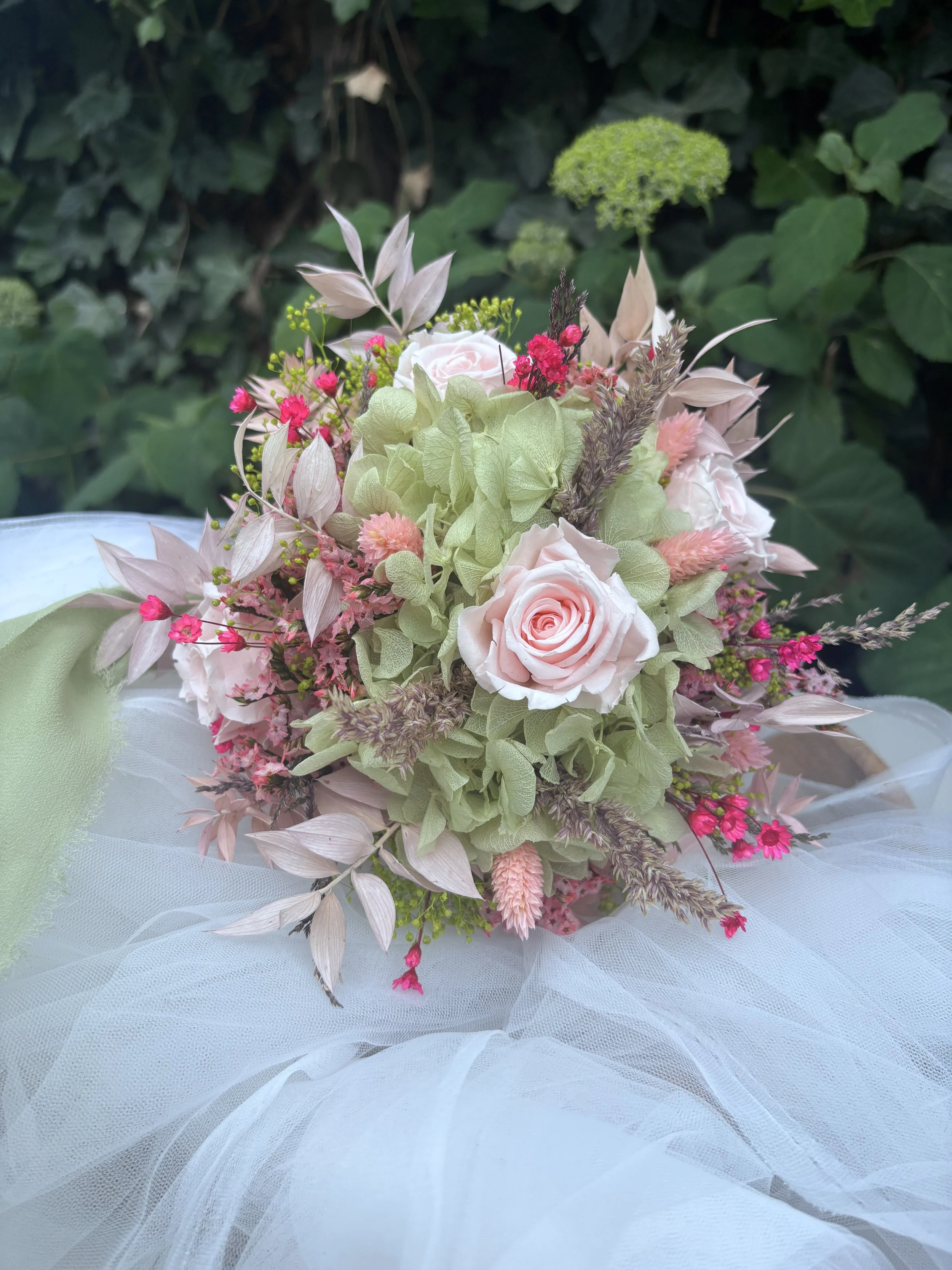 Bouquet de mariée en fleurs séchées et stabilisées aux tons rose poudré, vert sauge et beige naturel, réalisé à la main par L’Atelier Fleurs & Sens près de Valenciennes. Cette création florale bohème et romantique associe hortensia stabilisé, roses s