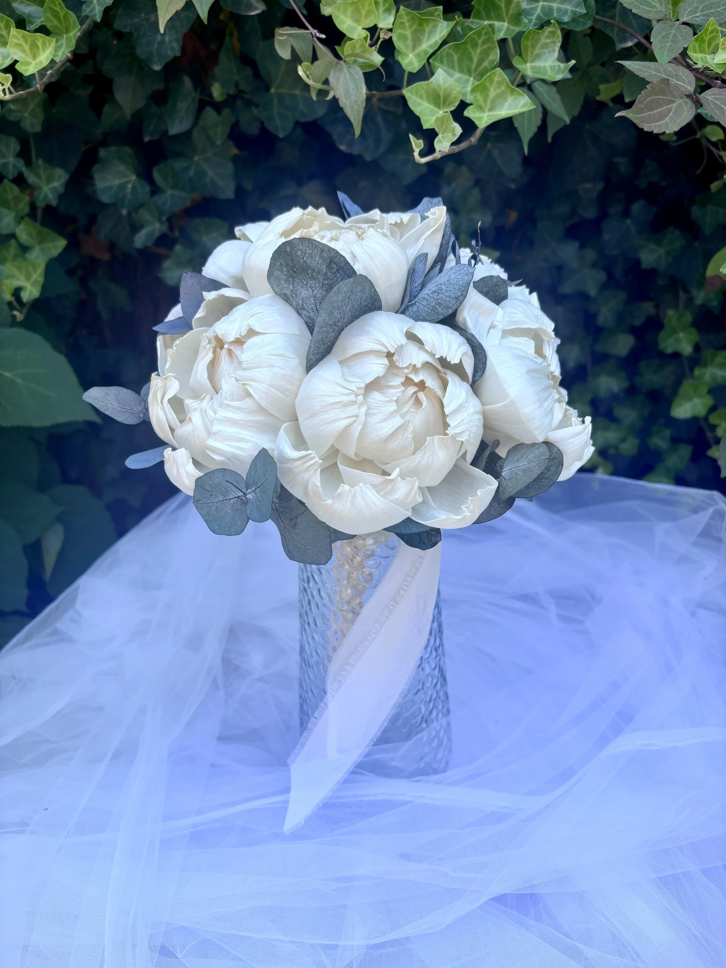 Bouquet de mariée élégant et intemporel composé de grandes pivoines ivoire en bois de Sola, associées à un feuillage d’eucalyptus. Une création florale durable, réalisée artisanalement et personnalisable selon les couleurs du mariage par L’Atelier Fl