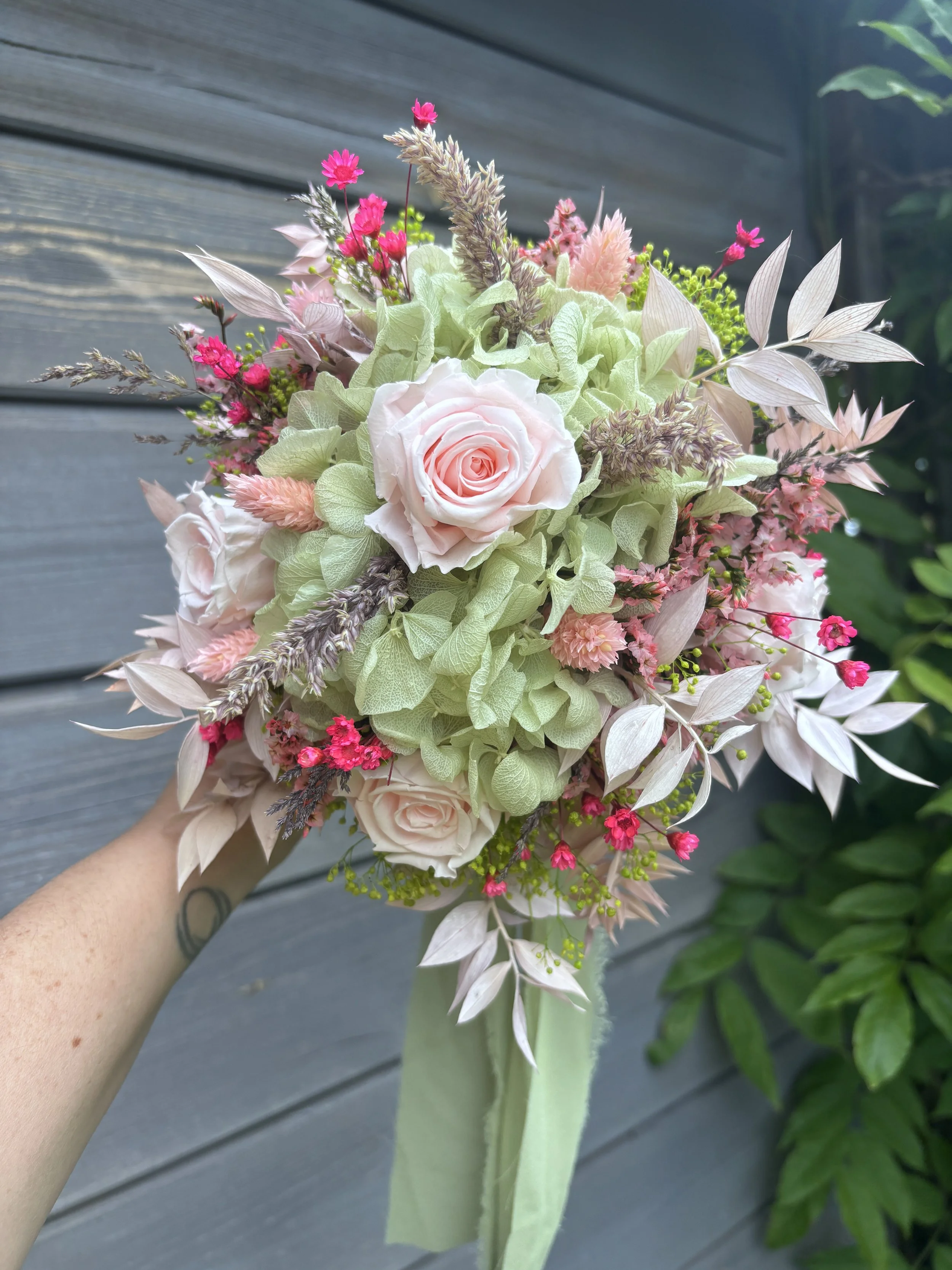 Bouquet de mariée en fleurs séchées et stabilisées aux tons rose poudré, vert sauge et beige naturel, réalisé à la main par L’Atelier Fleurs & Sens près de Valenciennes. Cette création florale bohème et romantique associe hortensia stabilisé, roses s