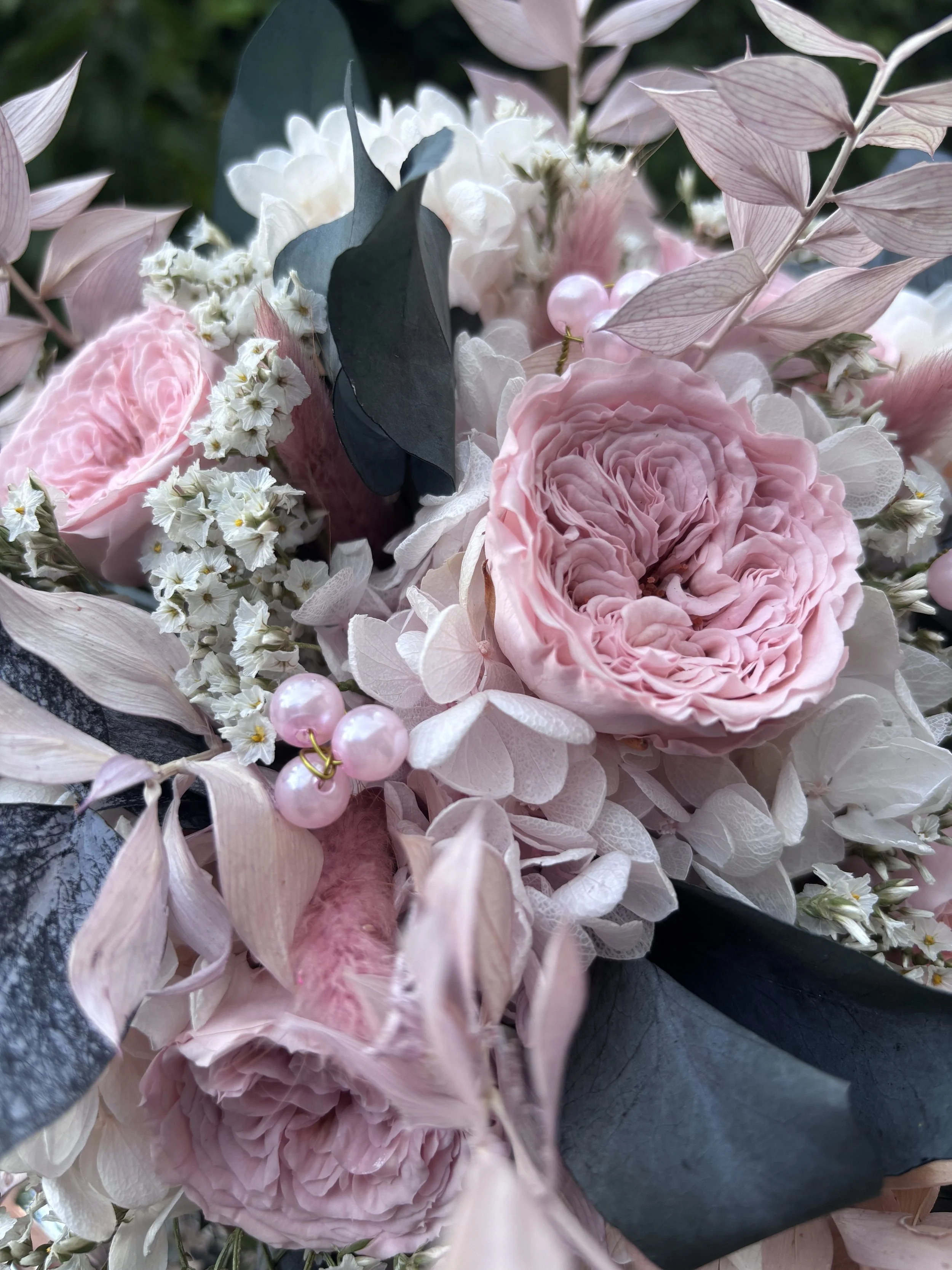 Bouquet de mariée bohème réalisé à la main en fleurs séchées et stabilisées dans des tons rose poudré, blanc et gris bleuté. Cette création florale associe de délicates roses anglaises stabilisées, des hortensias préservés, de l’eucalyptus et des feu