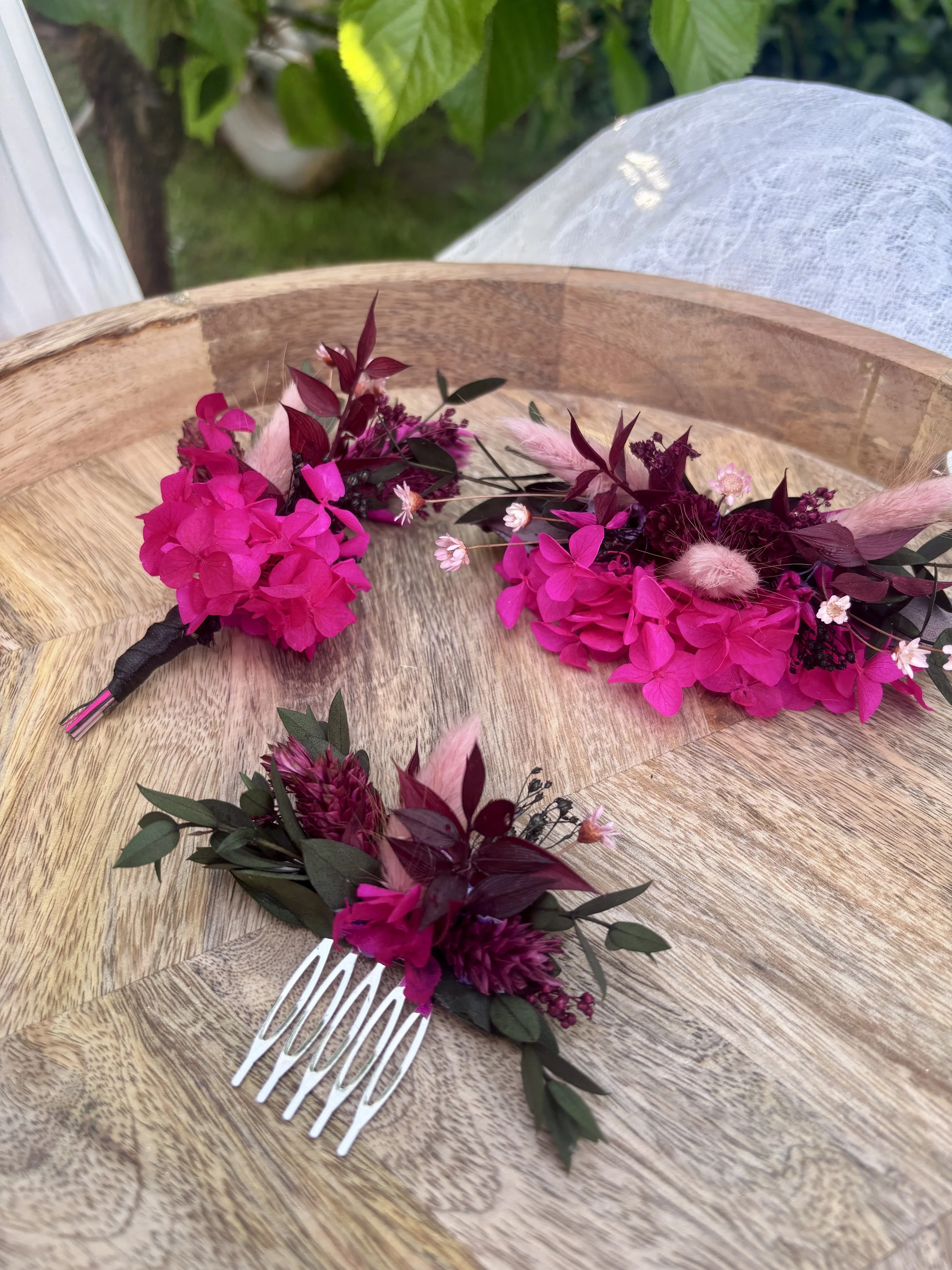 Couronne de fleurs violettes et roses avec branches de feuilles vertes, posée sur une table en bois