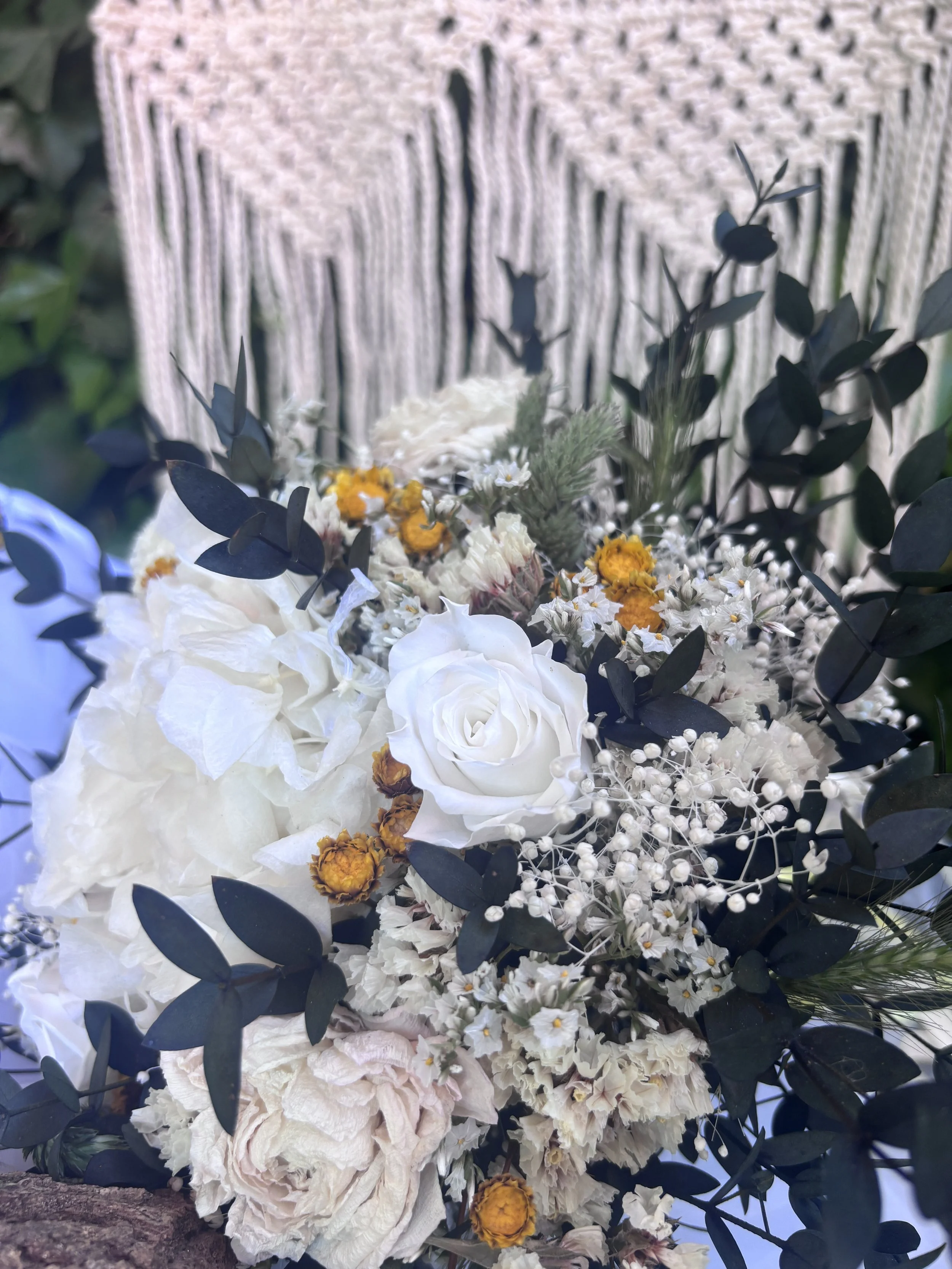 Bouquet de fleurs blanches, jaunes et verdâtres avec des feuilles vertes foncées, posé devant un fond en bois clair.