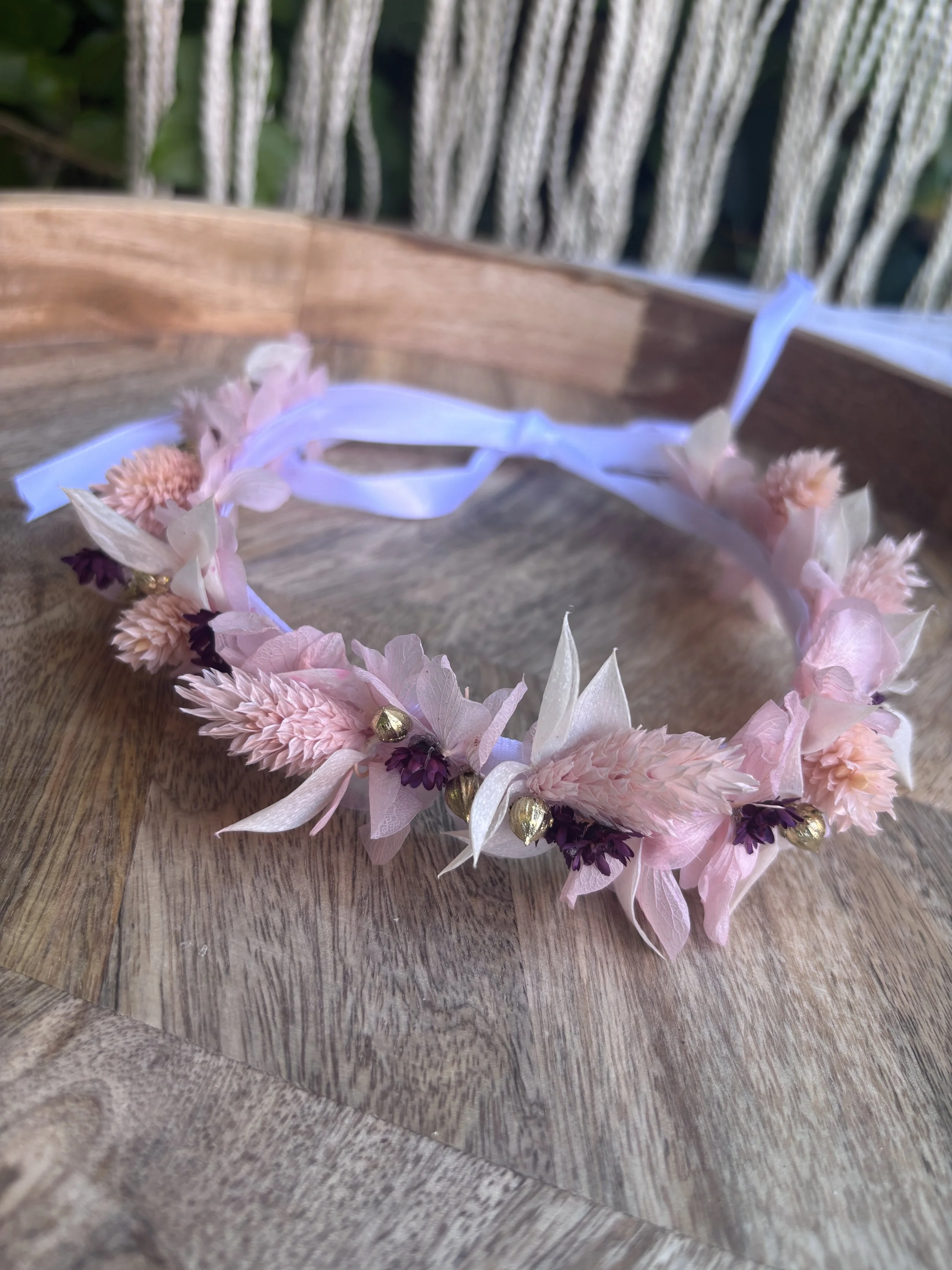 Couronne de fleurs en tissu rose, blanc et doré posée sur une surface en bois