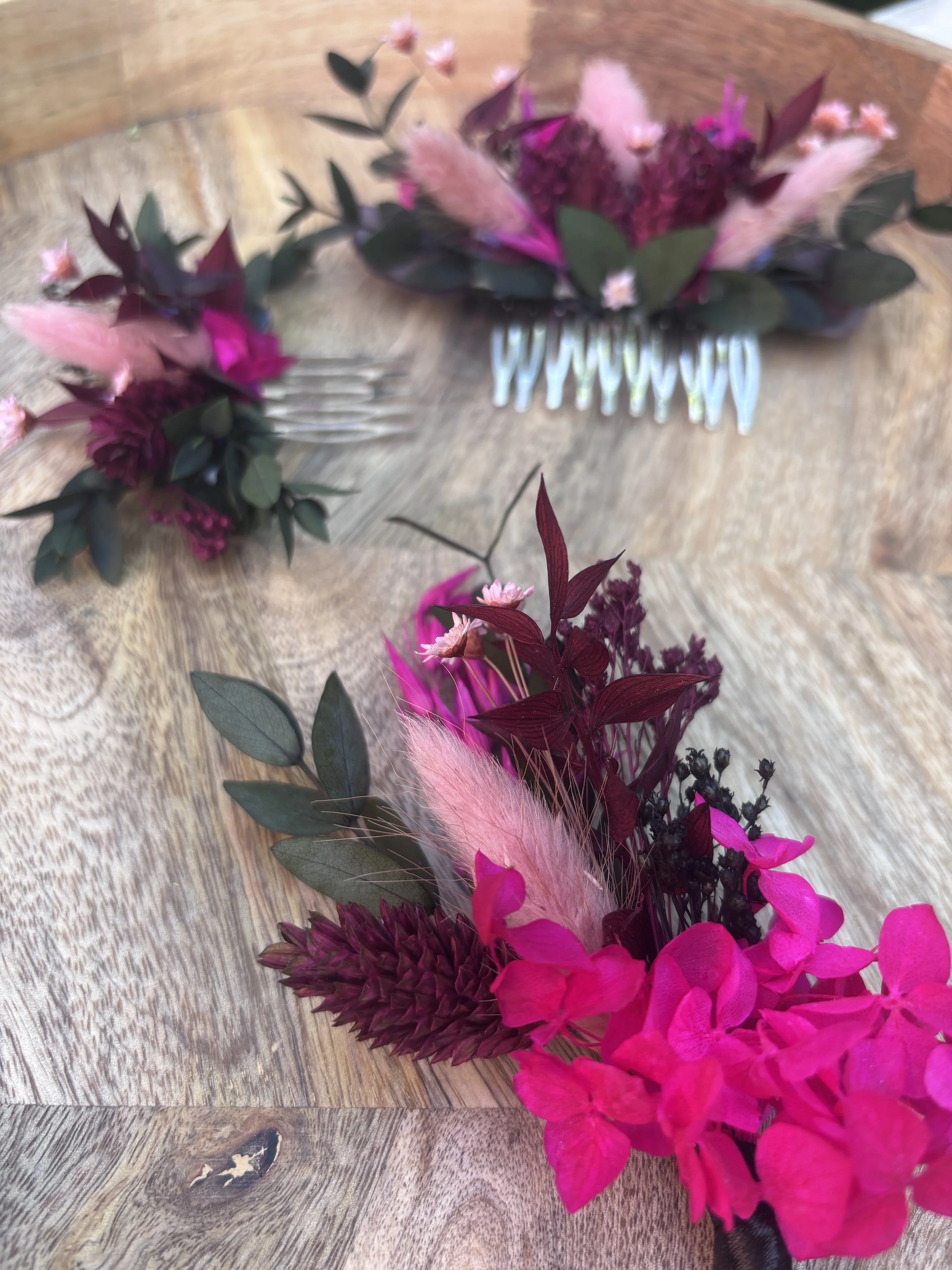Un bouquet de fleurs colorées avec du vert, du rose, du violet, du rouge et du fuchsia, placé sur une surface en bois.