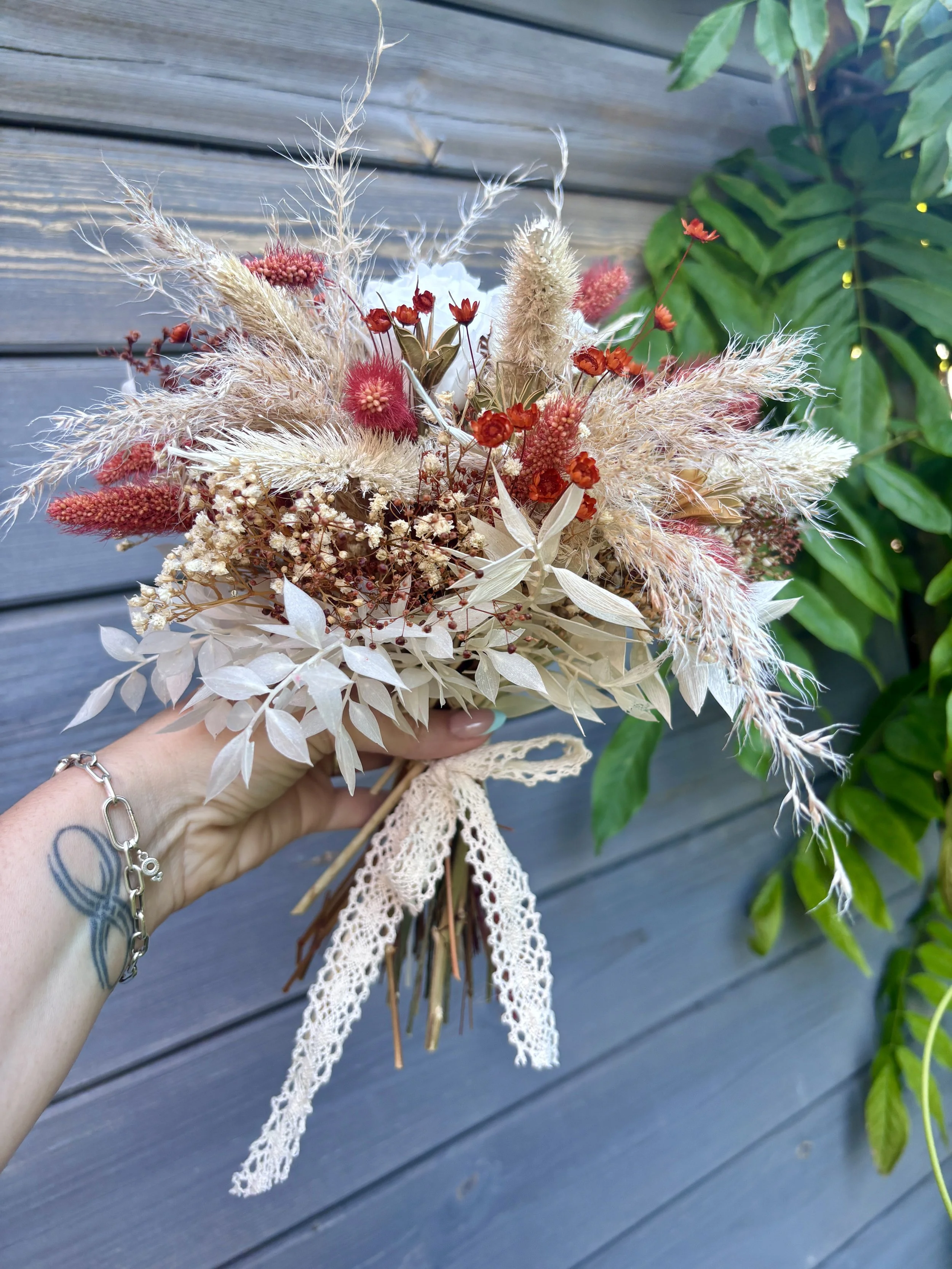 Bouquet de mariée bohème en fleurs séchées et stabilisées aux teintes terracotta, bordeaux, crème et blanc. Cette création florale artisanale associe roses éternelles blanches, pampas, setaria, graminées naturelles et délicates fleurs séchées pour of