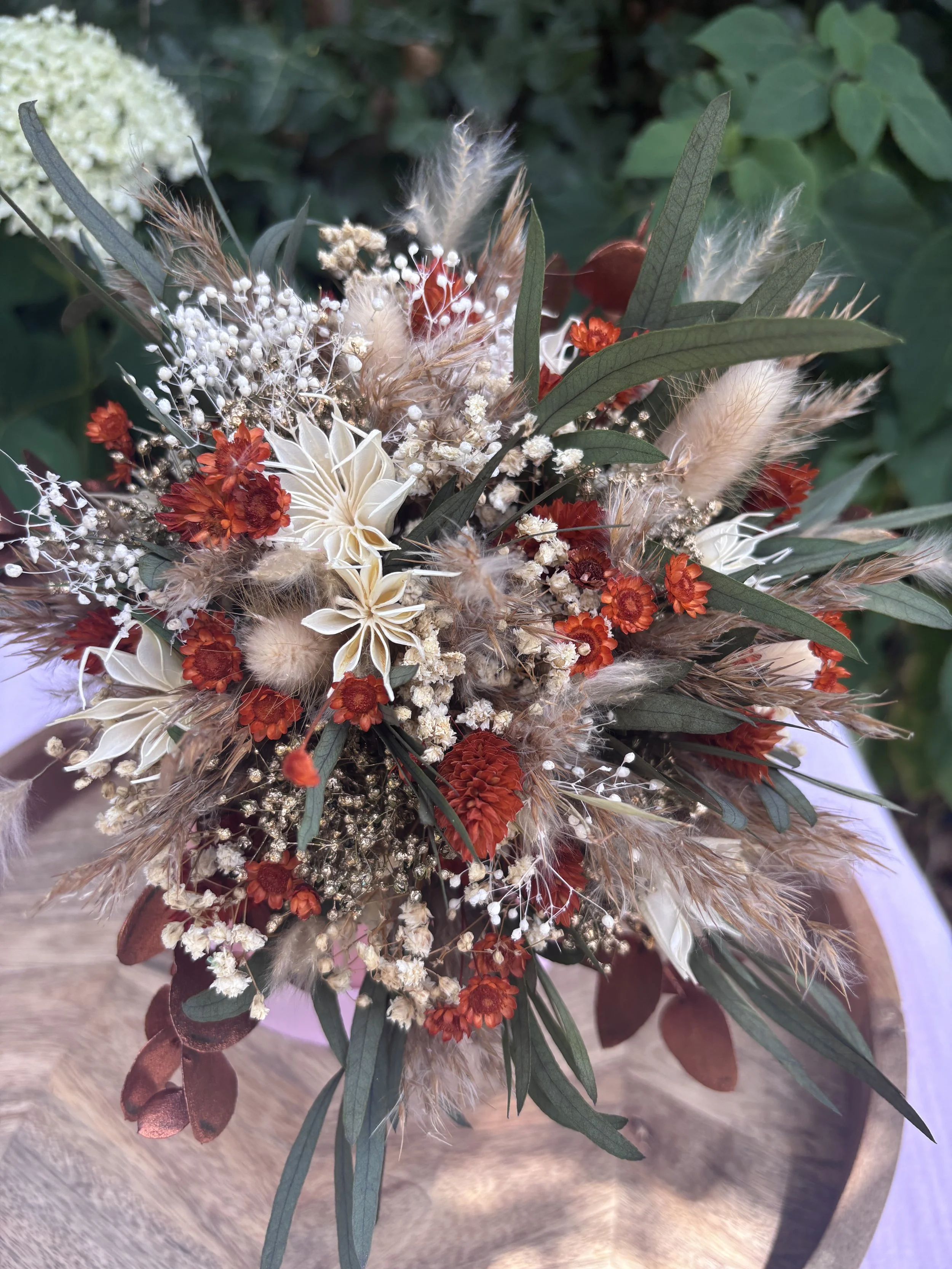 Bouquet de mariée en fleurs séchées et stabilisées dans un style bohème champêtre, composé de gypsophile, lagurus, eucalyptus, fleurs terracotta, touches crème et feuillages aux nuances bordeaux. Une création durable et naturelle, idéale pour un mari