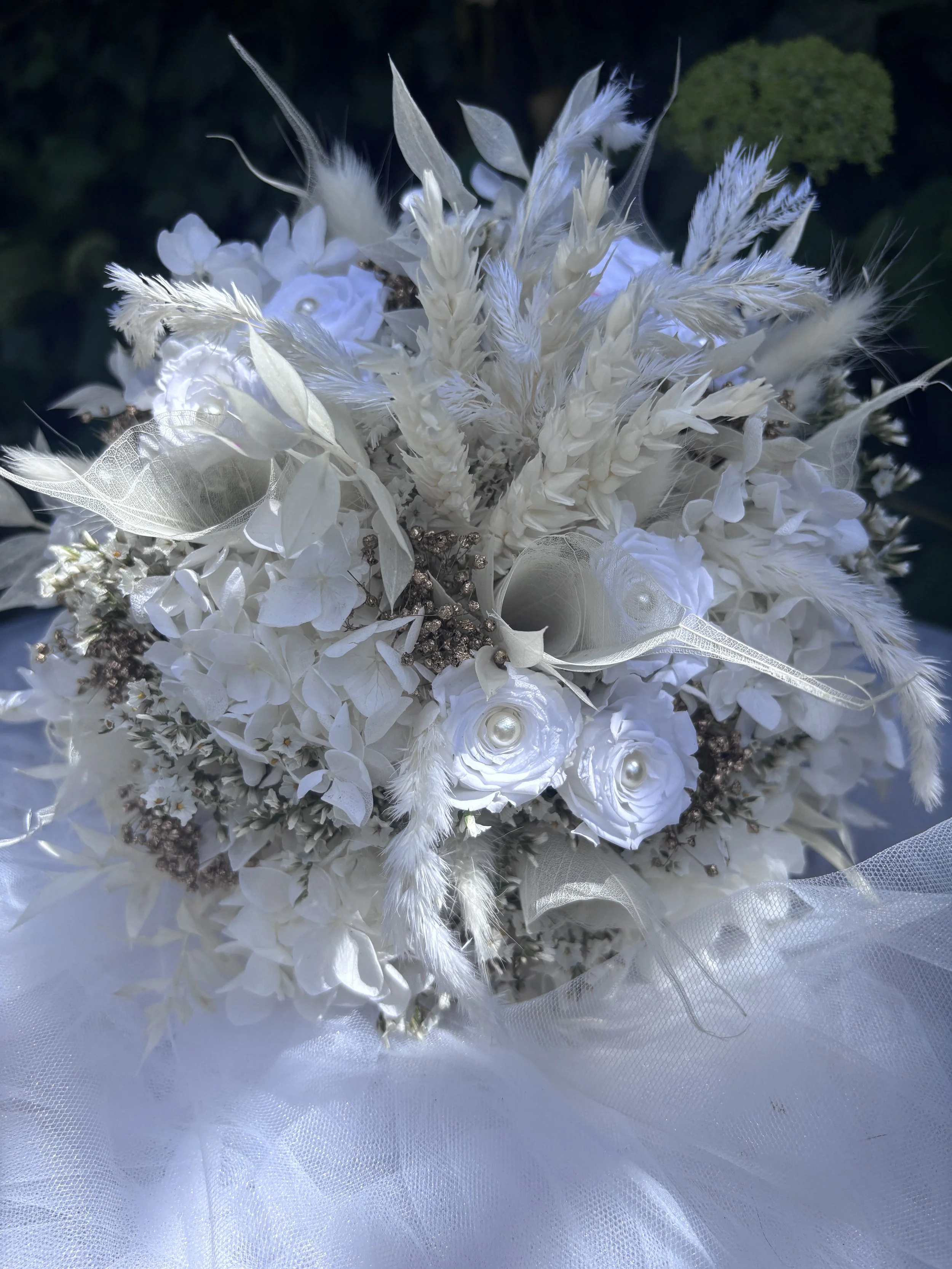 Ce bouquet de mariée en fleurs séchées et stabilisées associe hortensias blancs, renoncules stabilisées, graminées aériennes et délicates touches nacrées pour un rendu élégant, romantique et intemporel. Réalisé à la main dans mon atelier à Saint-Saul