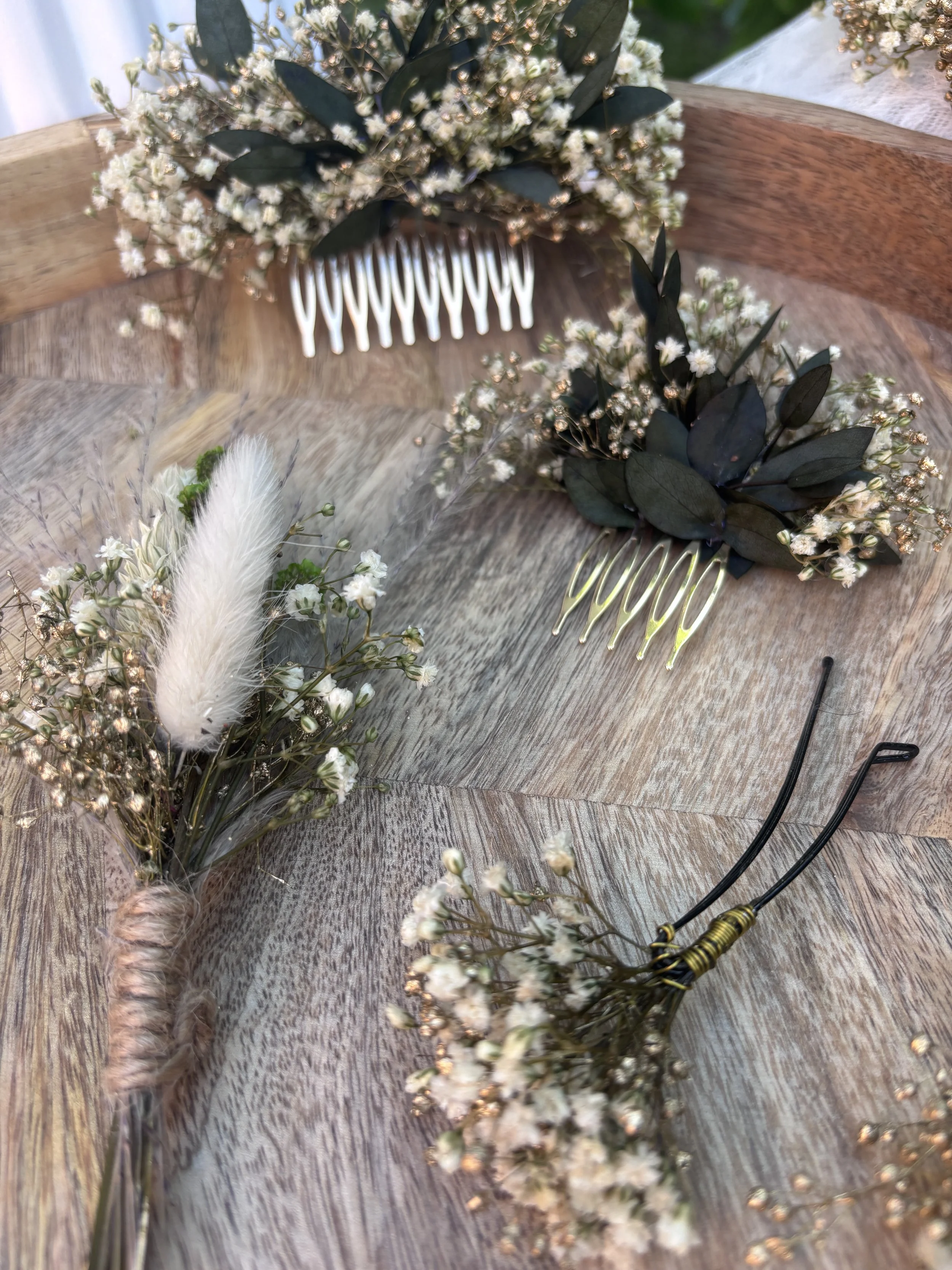 Compositions florales avec des fleurs blanches, des feuilles vertes et des accessoires de coiffure sur une table en bois