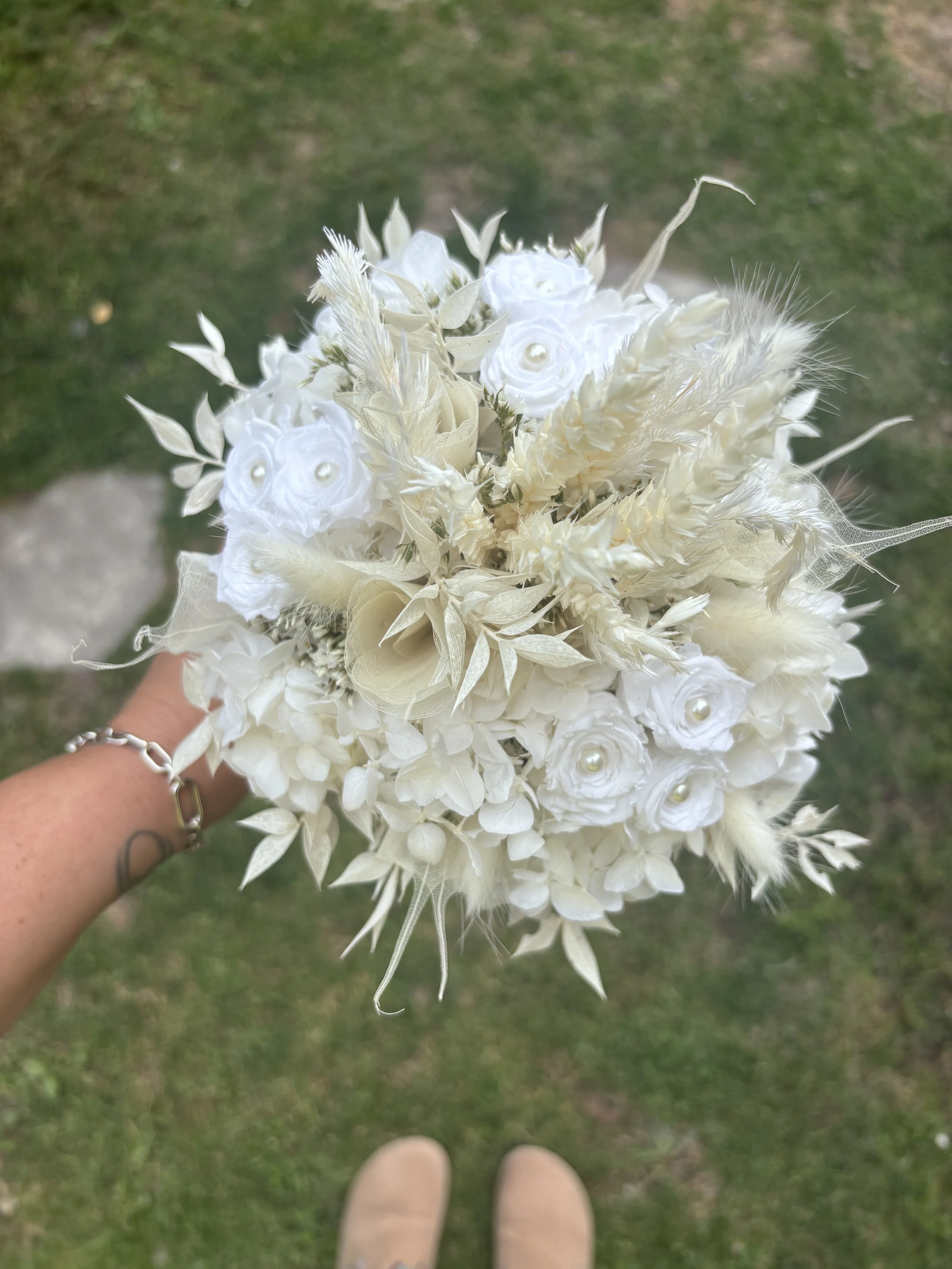 Bouquet de mariée en fleurs séchées et stabilisées blanches, réalisé artisanalement dans un esprit bohème chic et romantique. Cette création florale associe hortensias stabilisés, roses éternelles ornées de perles, arums délicats, feuillages blanchis