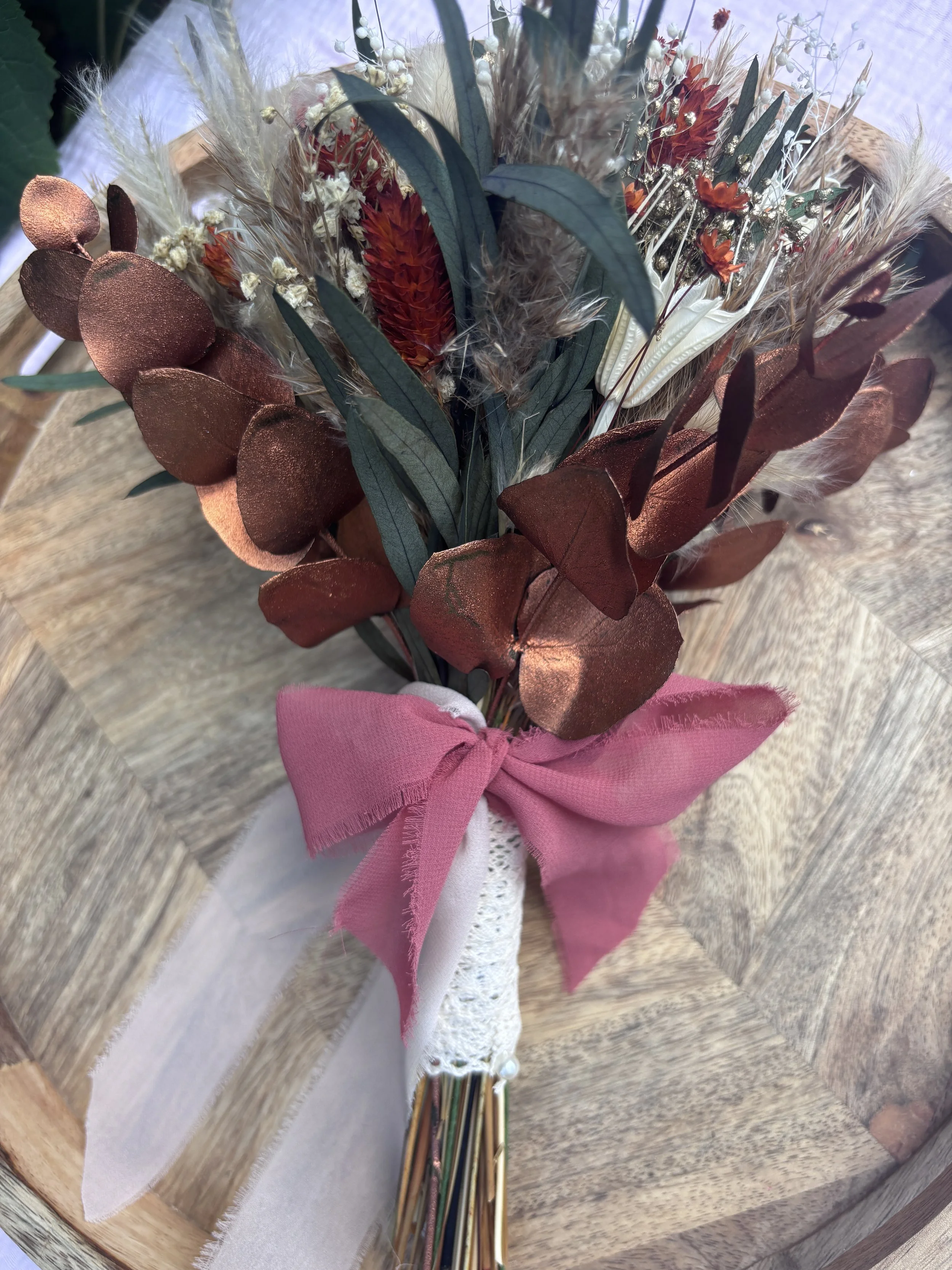 Bouquet de mariée en fleurs séchées et stabilisées dans un style bohème champêtre, composé de gypsophile, lagurus, eucalyptus, fleurs terracotta, touches crème et feuillages aux nuances bordeaux. Une création durable et naturelle, idéale pour un mari