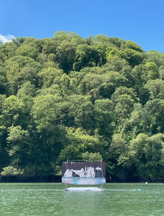 A floating screen displays a painting of icebergs and water, set against a backdrop of lush green trees on a hillside under a clear blue sky.