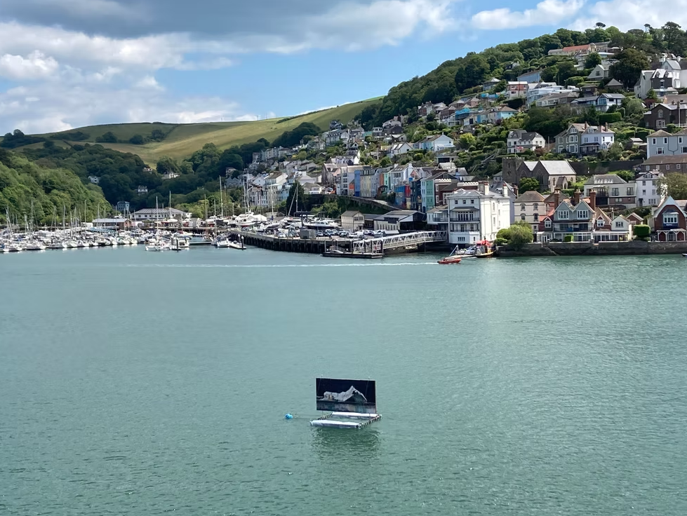 Harbor with numerous boats docked, colorful houses on a hillside, and a partly cloudy sky.