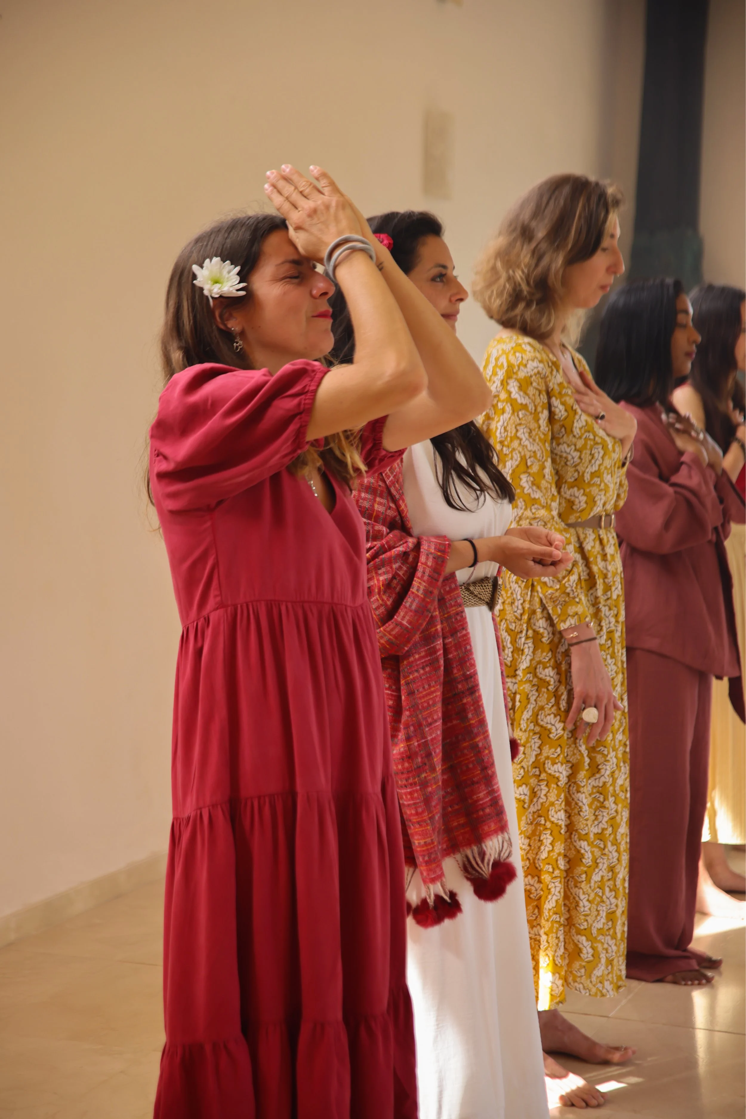Grupo de mujeres en oración con ojos cerrados, algunas con mano en el corazón, en una línea, en un lugar interior con luz suave.