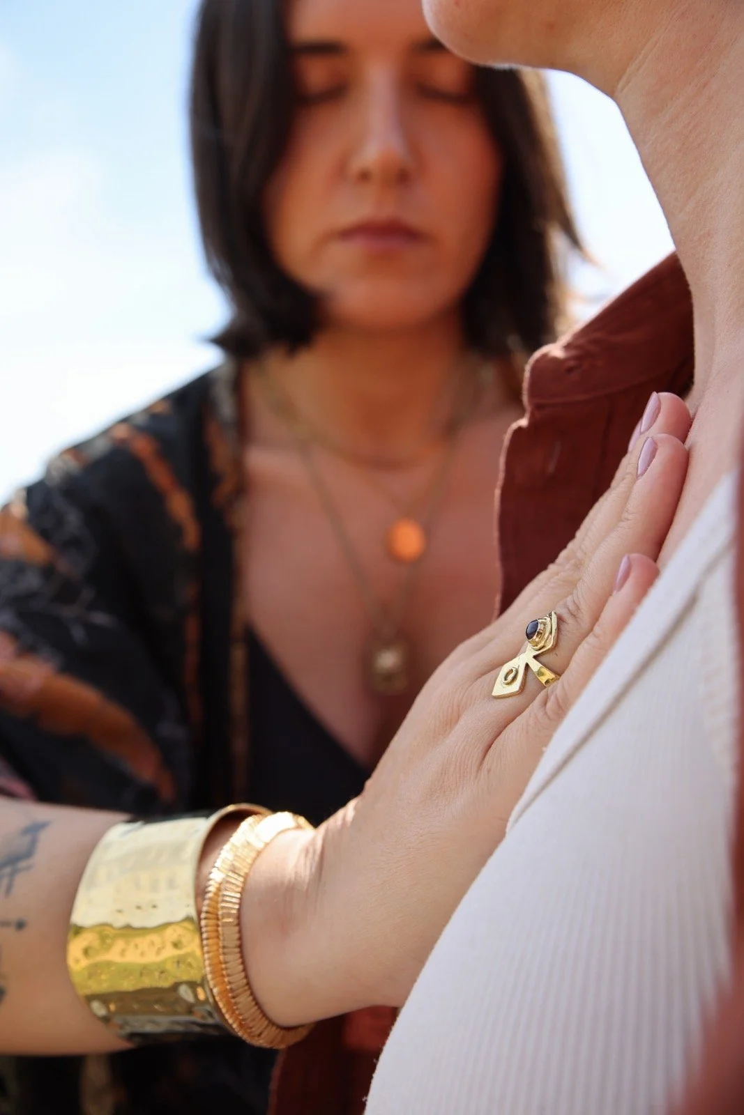 Mujer con joyas tocando el pecho de otra persona, con enfoque en la mano y el anillo, fondo desenfocado de rostro de mujer.