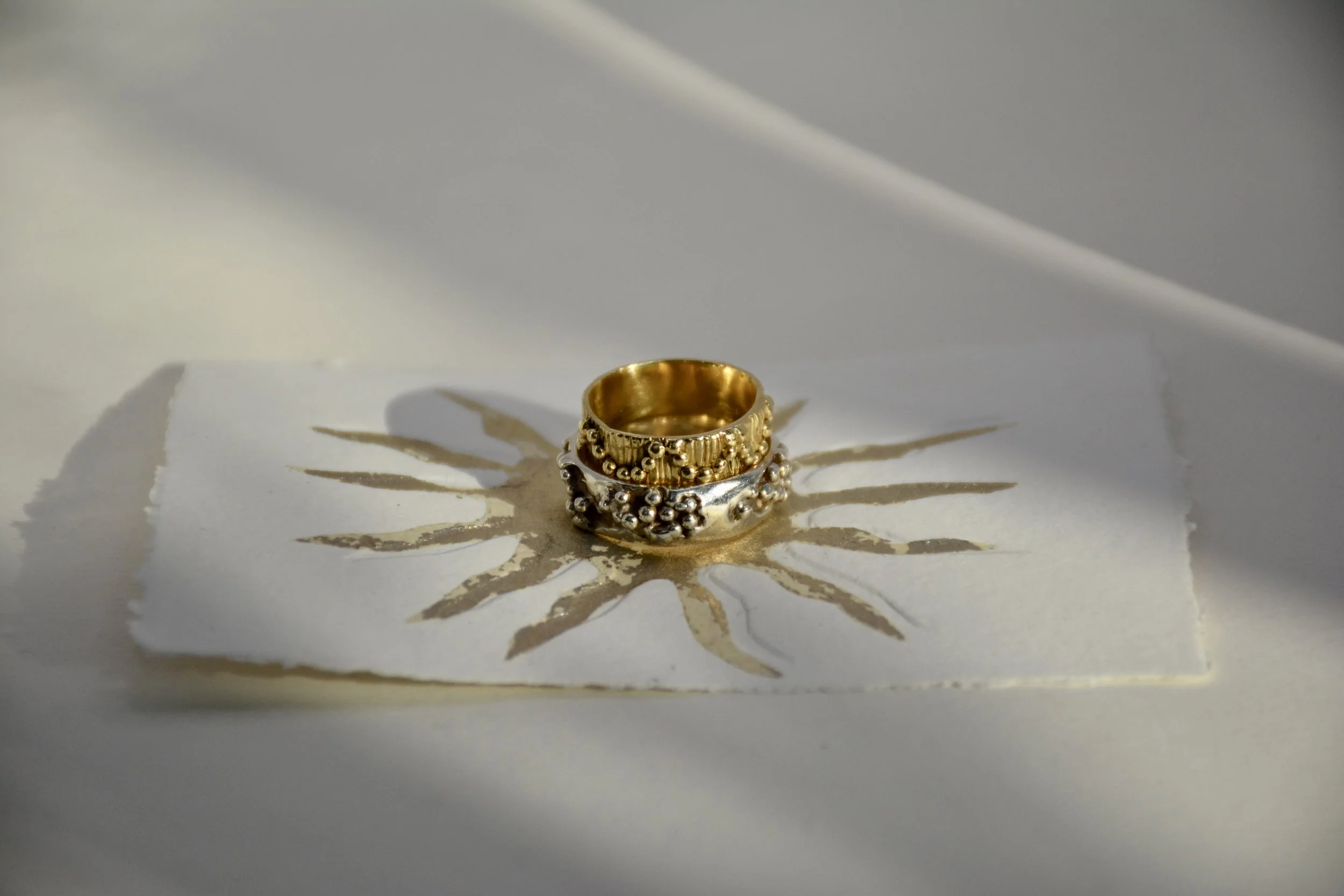 Deux anneaux or et agent, sur le soleil baroque du logo Vallmì