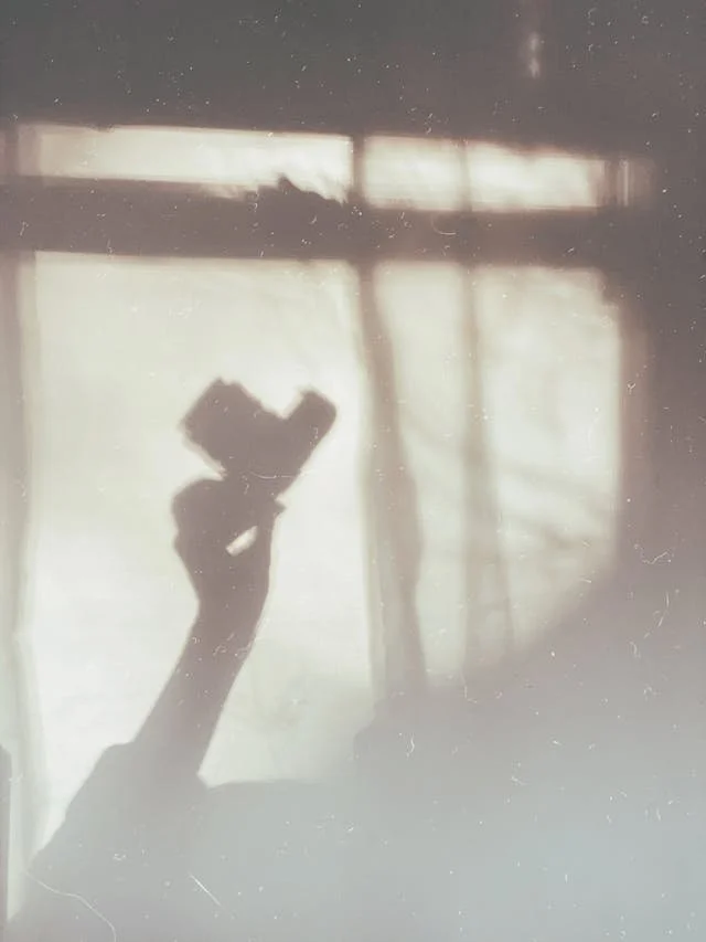 Shadow of a hand holding a smartphone in front of a window with curtains