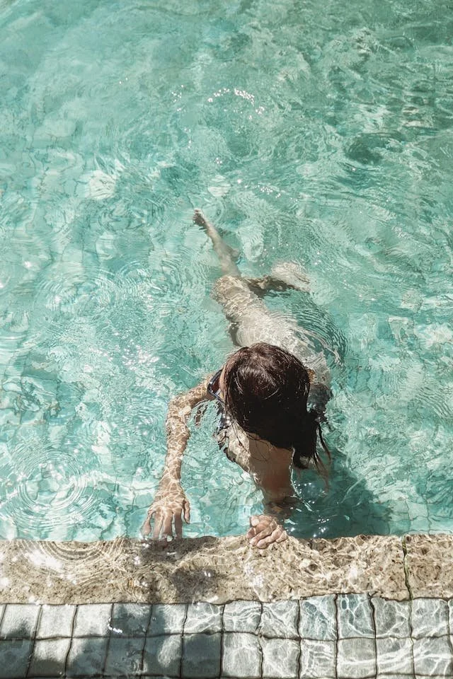 Child swimming in a pool, holding on to the edge with her hand.