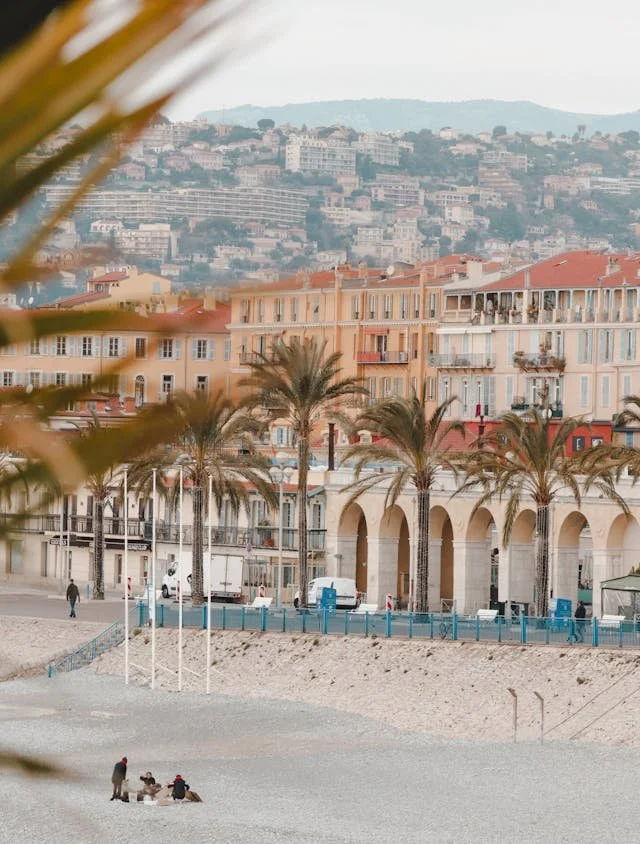 People on a beach with palm trees, colorful buildings, and a hillside in the background.