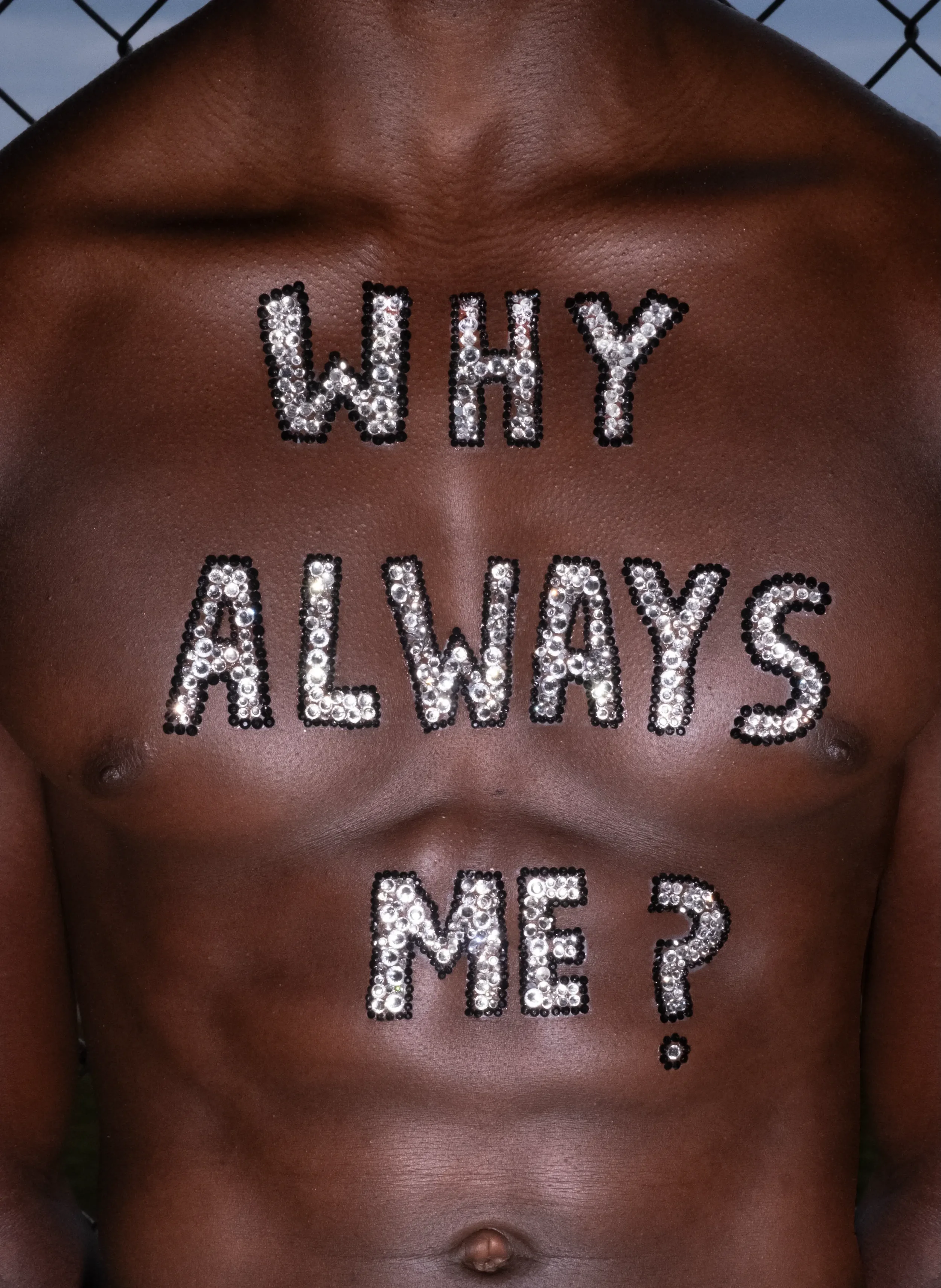 A person's chest with the words 'WHY ALWAYS ME' written in rhinestones.