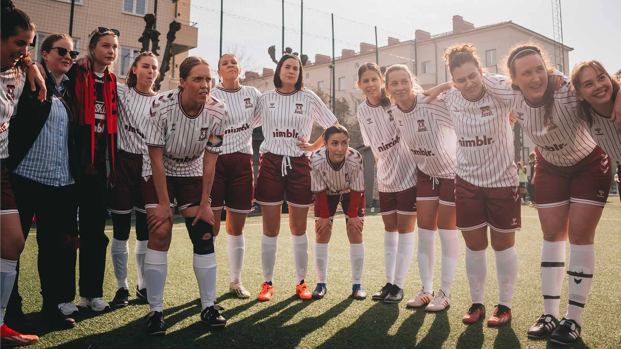 Group of female soccer players in white and maroon uniforms standing in a row on a soccer field.