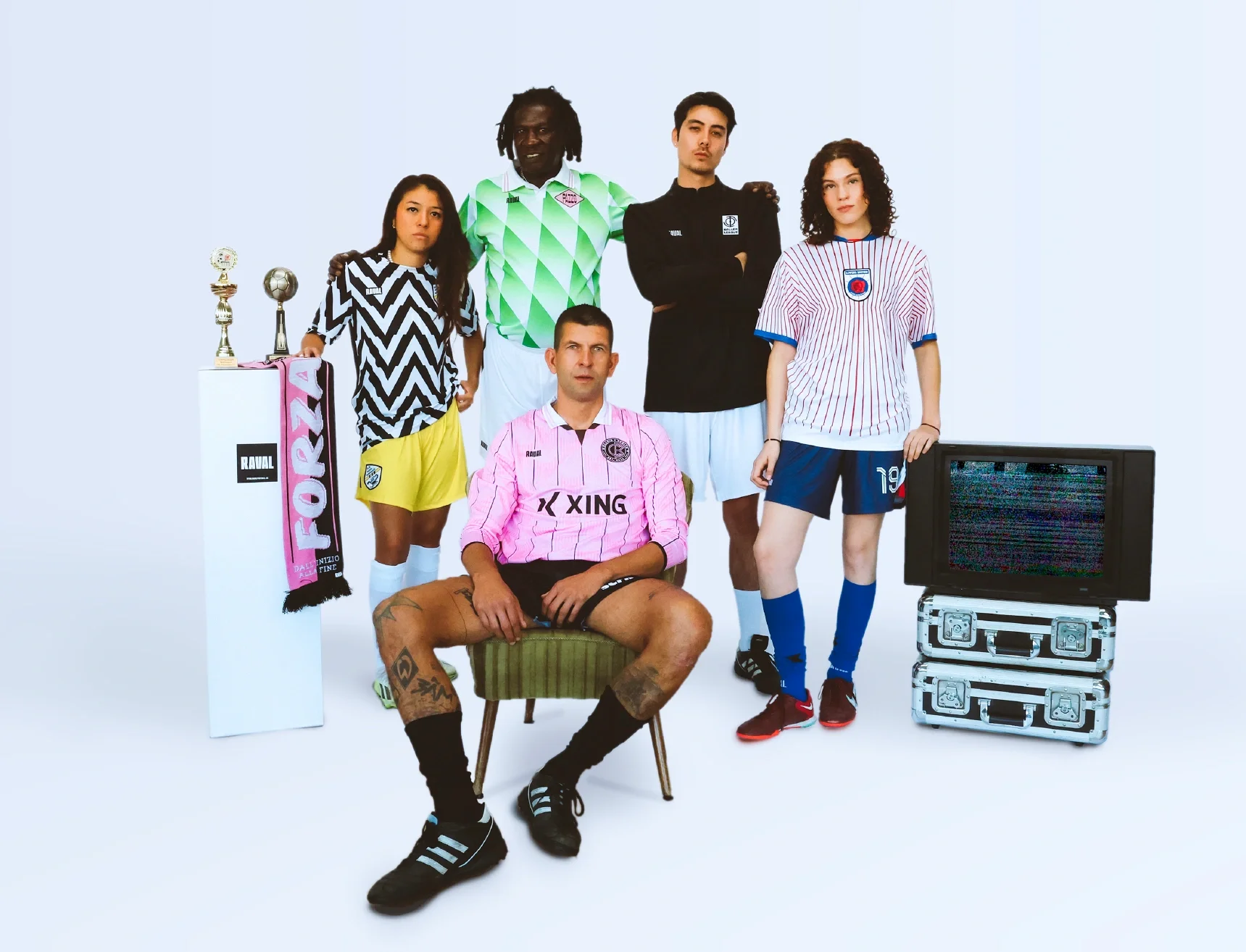 Five young adults in sportswear and jerseys, with two trophies and a scarf on display, standing and sitting beside a vintage TV on a plain white background.