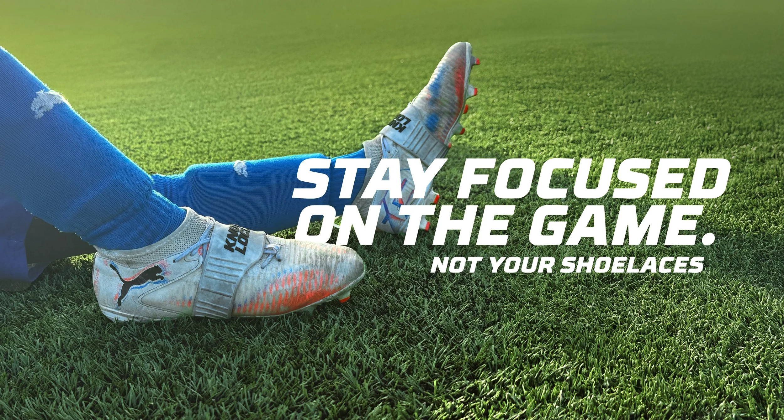 Close-up of soccer cleats, blue socks, and a player's foot on a grassy field with an inspirational message about focusing on the game, not shoes.