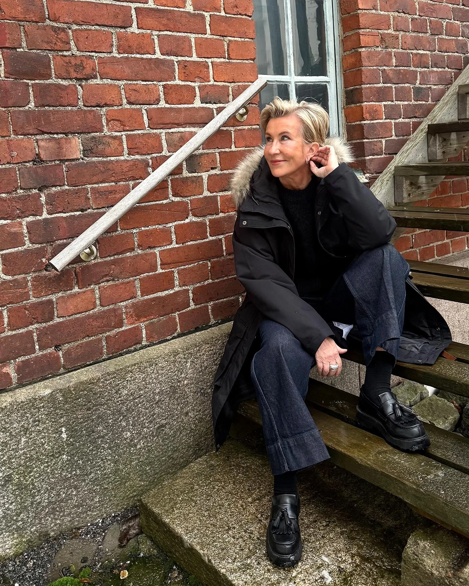 Leena Periaho istuu punaisen tiilirakennuksen edessä portailla.