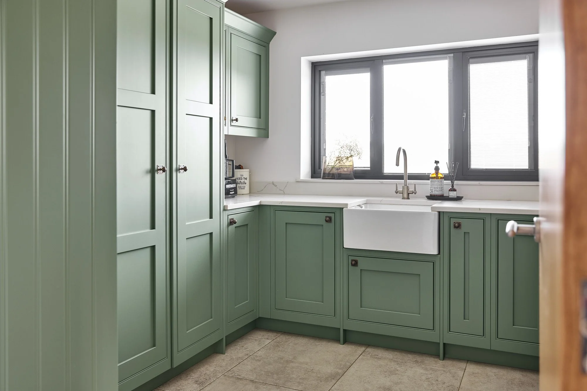 A kitchen with green cabinets, a white farmhouse sink, and a large window above the sink.