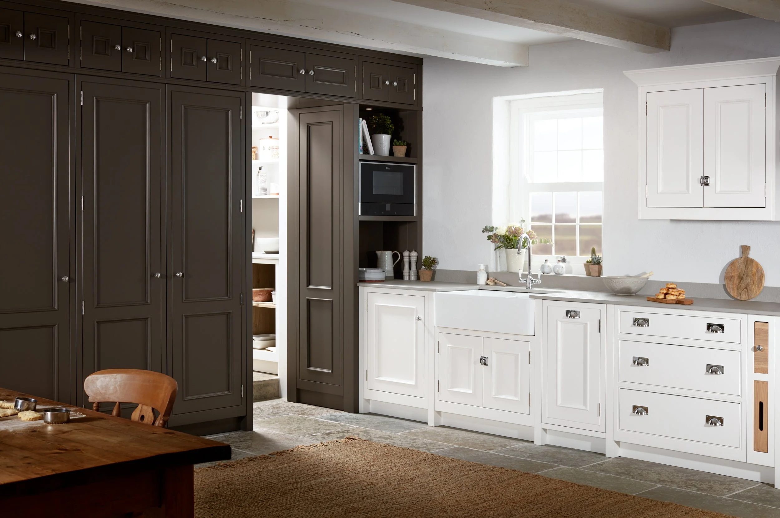 A cozy kitchen with white cabinets, a farmhouse sink, a window with a scenic view, and dark cabinetry with open pantry shelves.