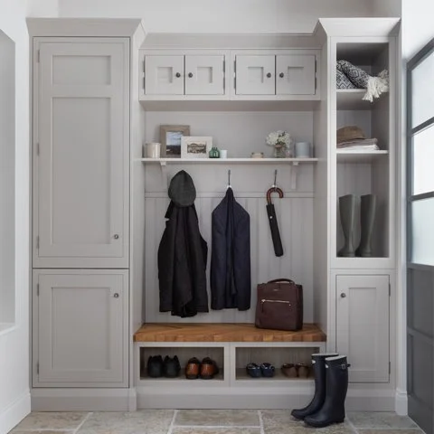 A white built-in closet with cabinets, shelves, and hooks, holding coats, shoes, and accessories, located by a window.