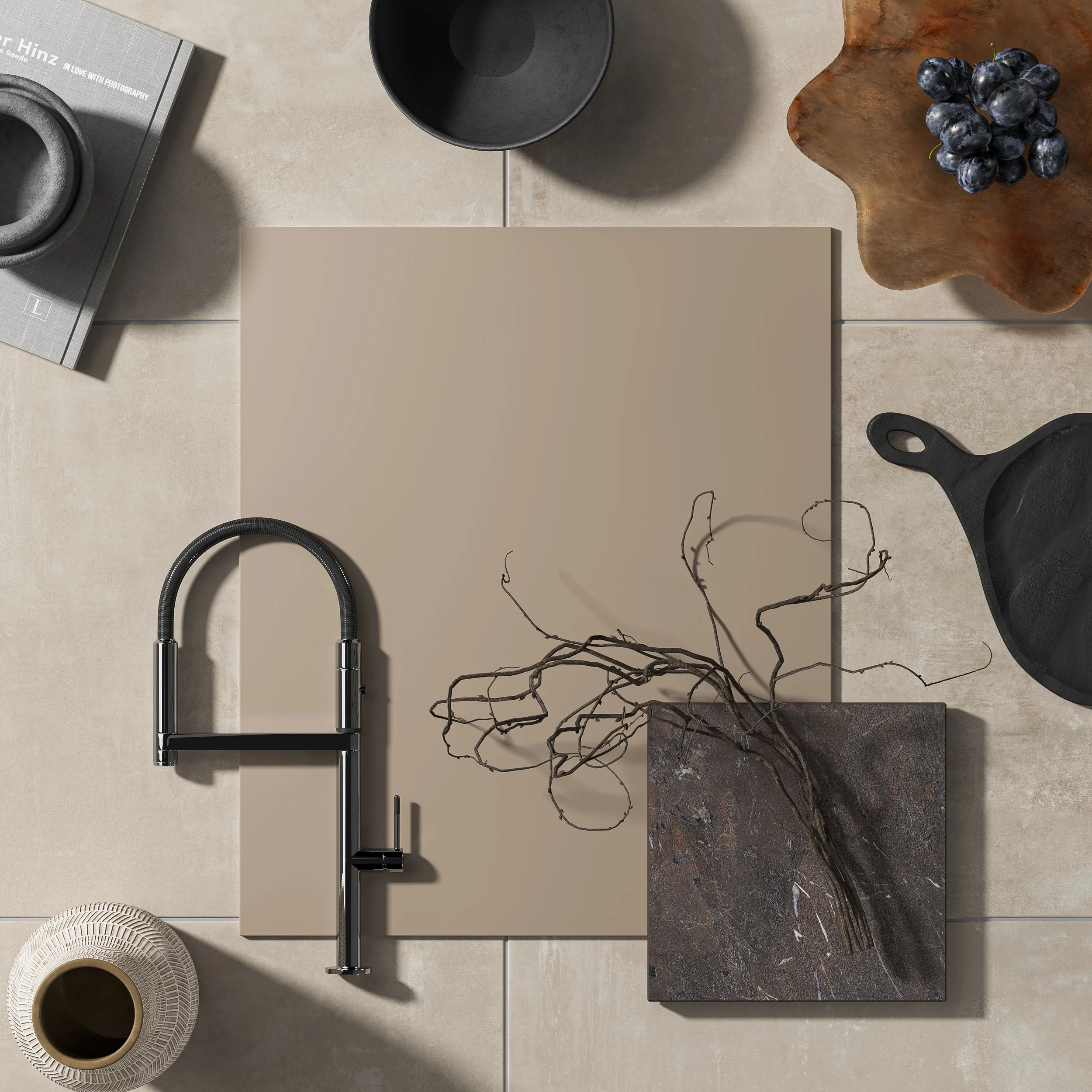Flat lay of modern kitchen and dining items, including a black faucet, a paint swatch, a branch on a marble tile, grapes on a wooden tray, black bowls, a cup, and a magazine.