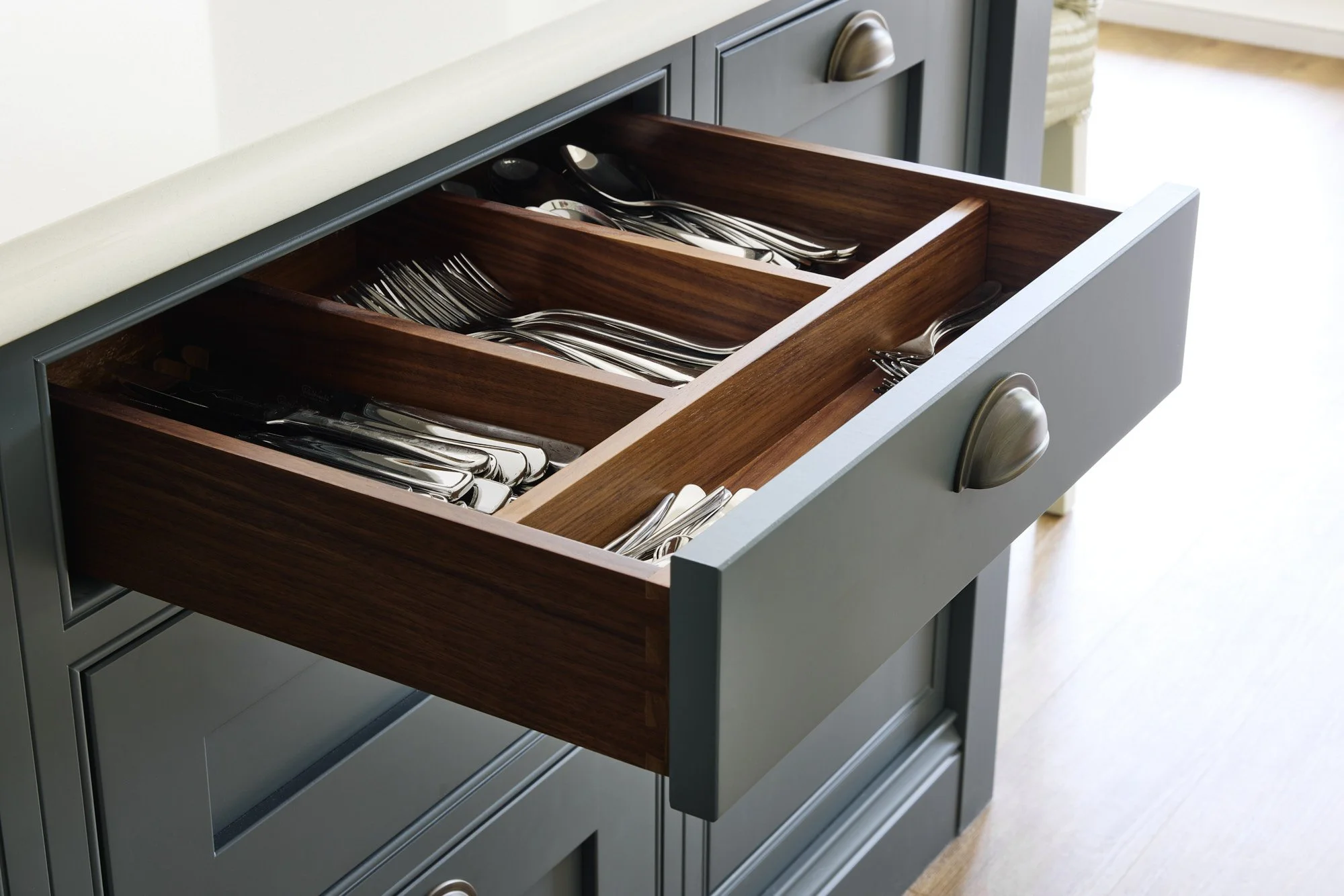 Open kitchen drawer filled with silverware including spoons, forks, and knives, organized in wooden divider compartments.