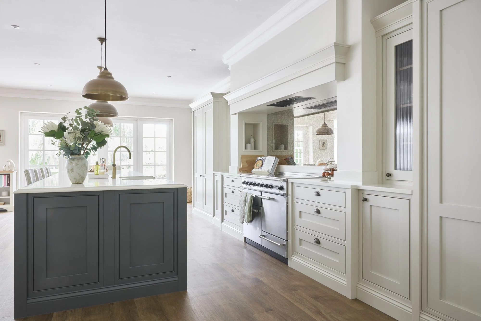 Bright kitchen with white cabinetry, a gray island with a vase of flowers, a stainless steel oven, and large windows letting in natural light.