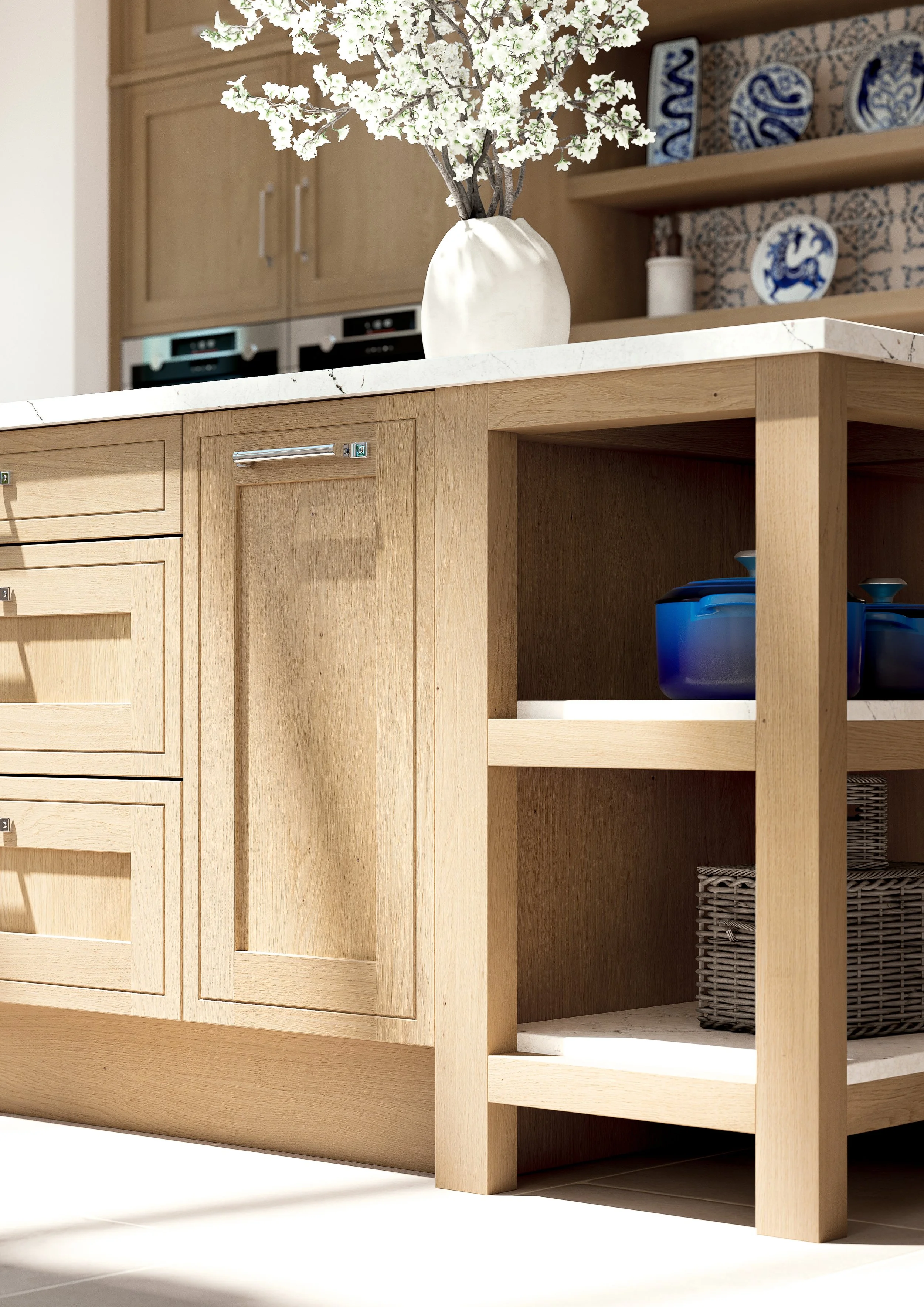 Close-up of a modern kitchen island with light wood cabinetry, a white marble countertop, and decorative items including a white vase with white flowers on top and blue ceramic bowls and plates on background shelves.