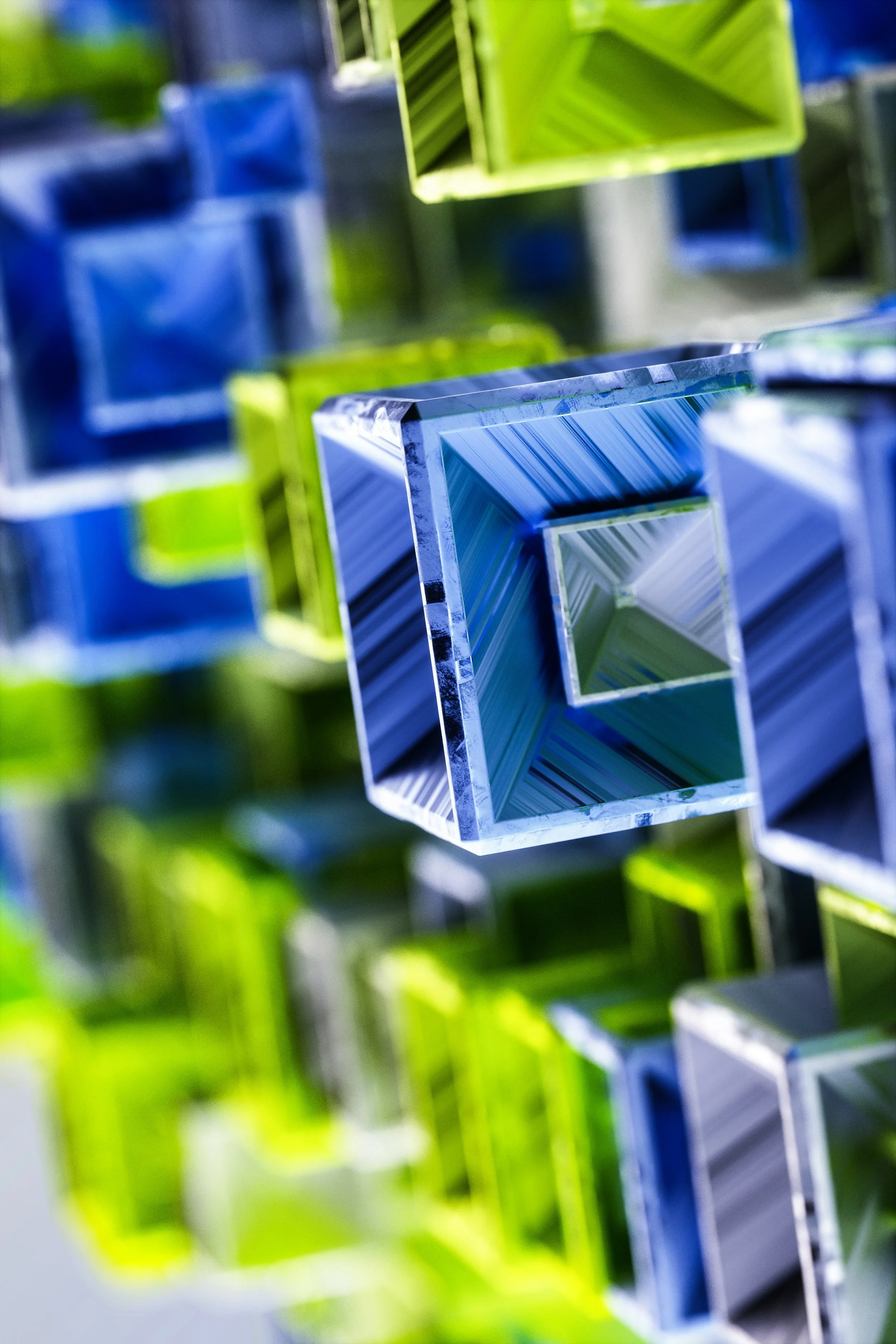 Close-up of colorful square glass tubes, with some colored green and blue, arranged in a pattern, reflecting light.