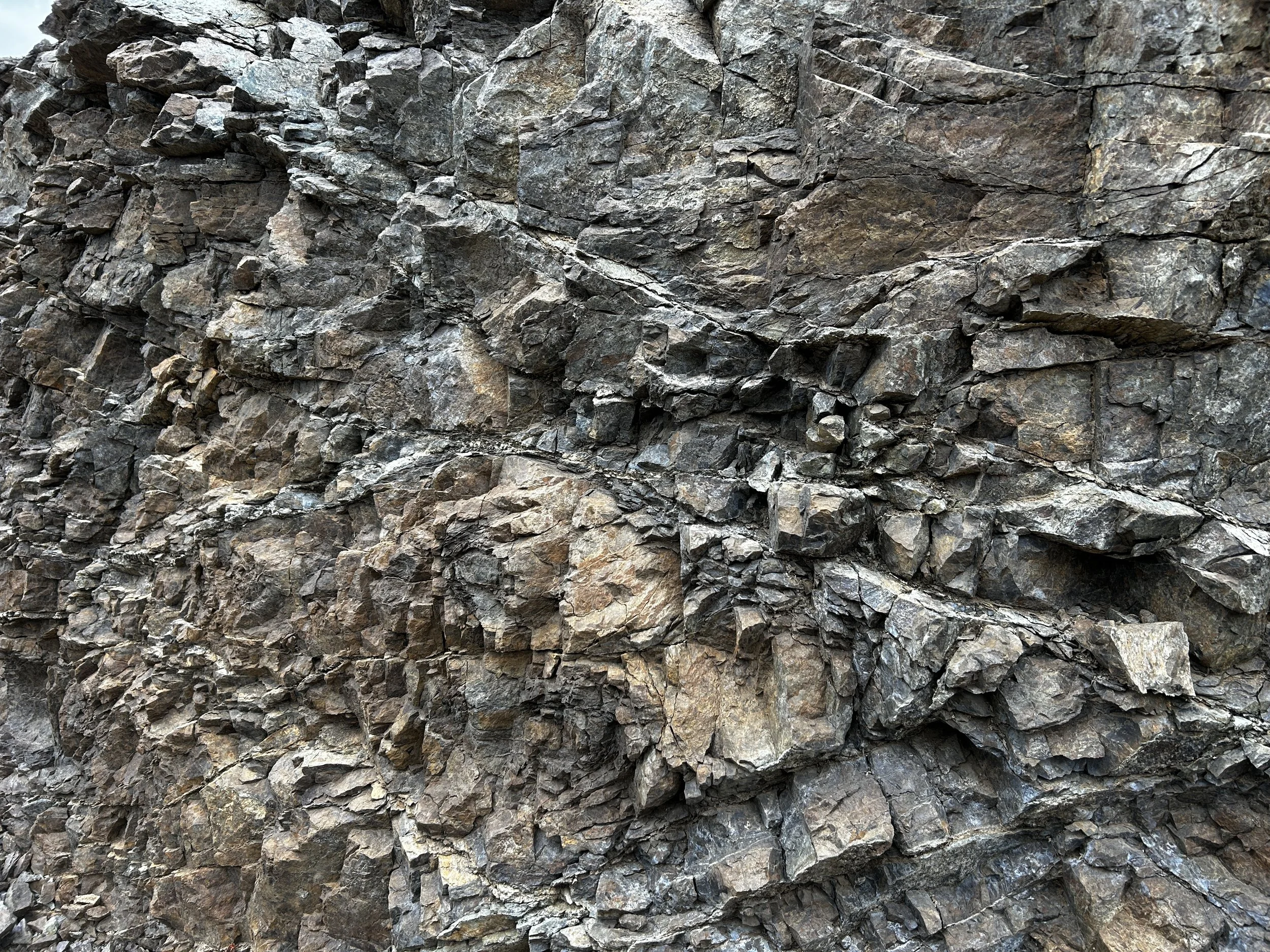 A close-up view of a rugged rock face with layered, jagged, gray and brown stones and cracks.