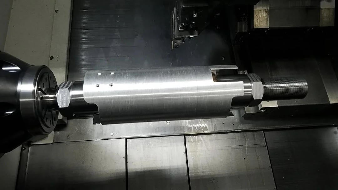 Metal machine part with threaded rod and cylindrical components in a workshop setting.