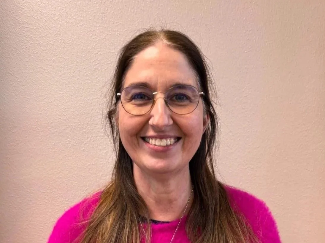 Lächelnde Frau mit Brille und braunen Haaren vor einem beige leinen Wand