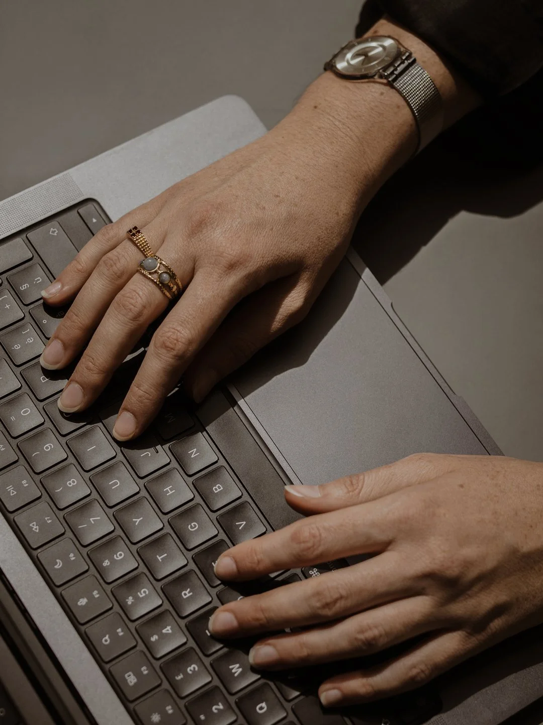 Mani femminili che digitano su una tastiera di un computer portatile, indossando anelli e un orologio