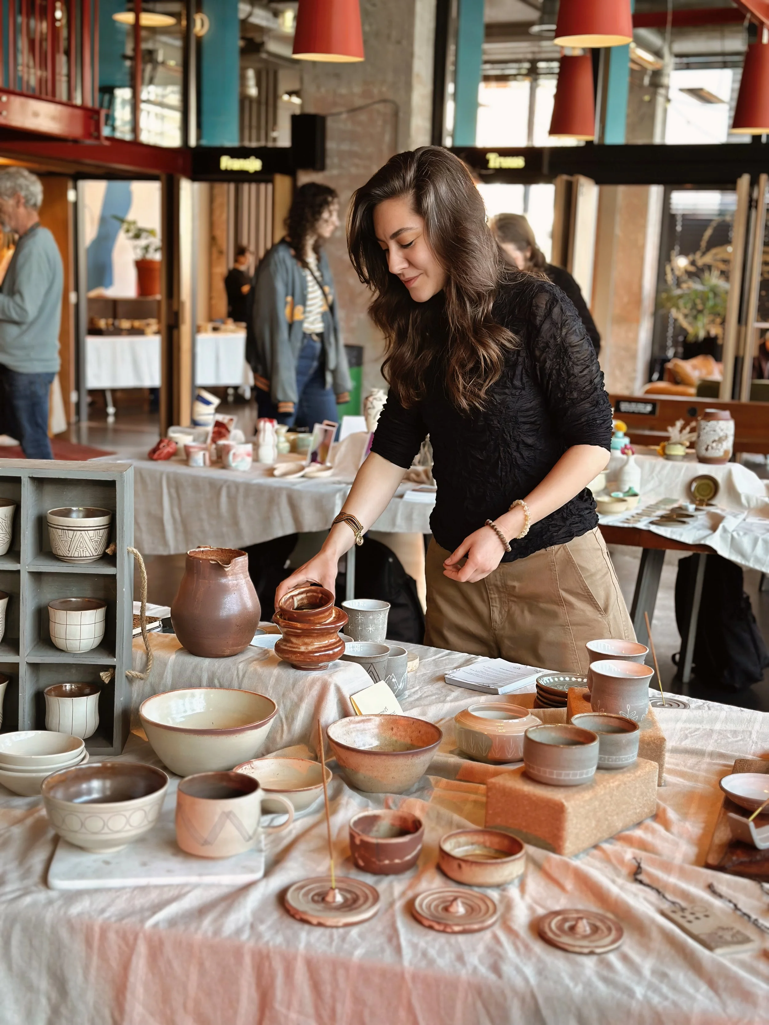 Woman selling ceramic pottery at an indoor market or art and craft fair.