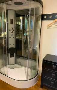 A modern, enclosed shower with glass doors and built-in controls in a bathroom, next to a black dresser and a wall hook with a hanger.